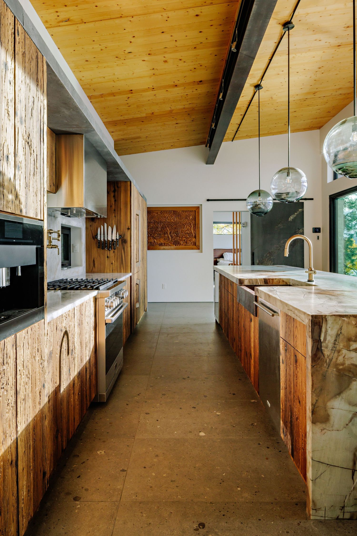Modern rustic kitchen with wooden cabinets, concrete floors, and glass pendant lights featuring a sleek island and stainless appliances.