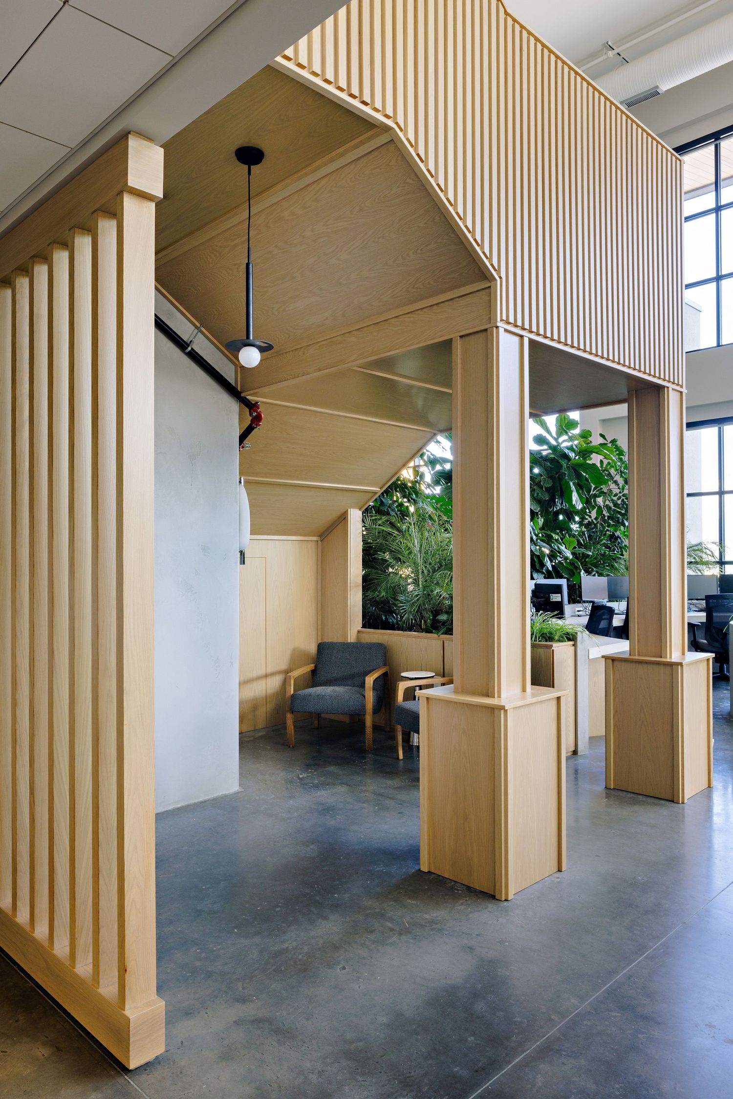 Light wood architectural feature with vertical slats creates an arched walkway in a modern office space with polished concrete floors.