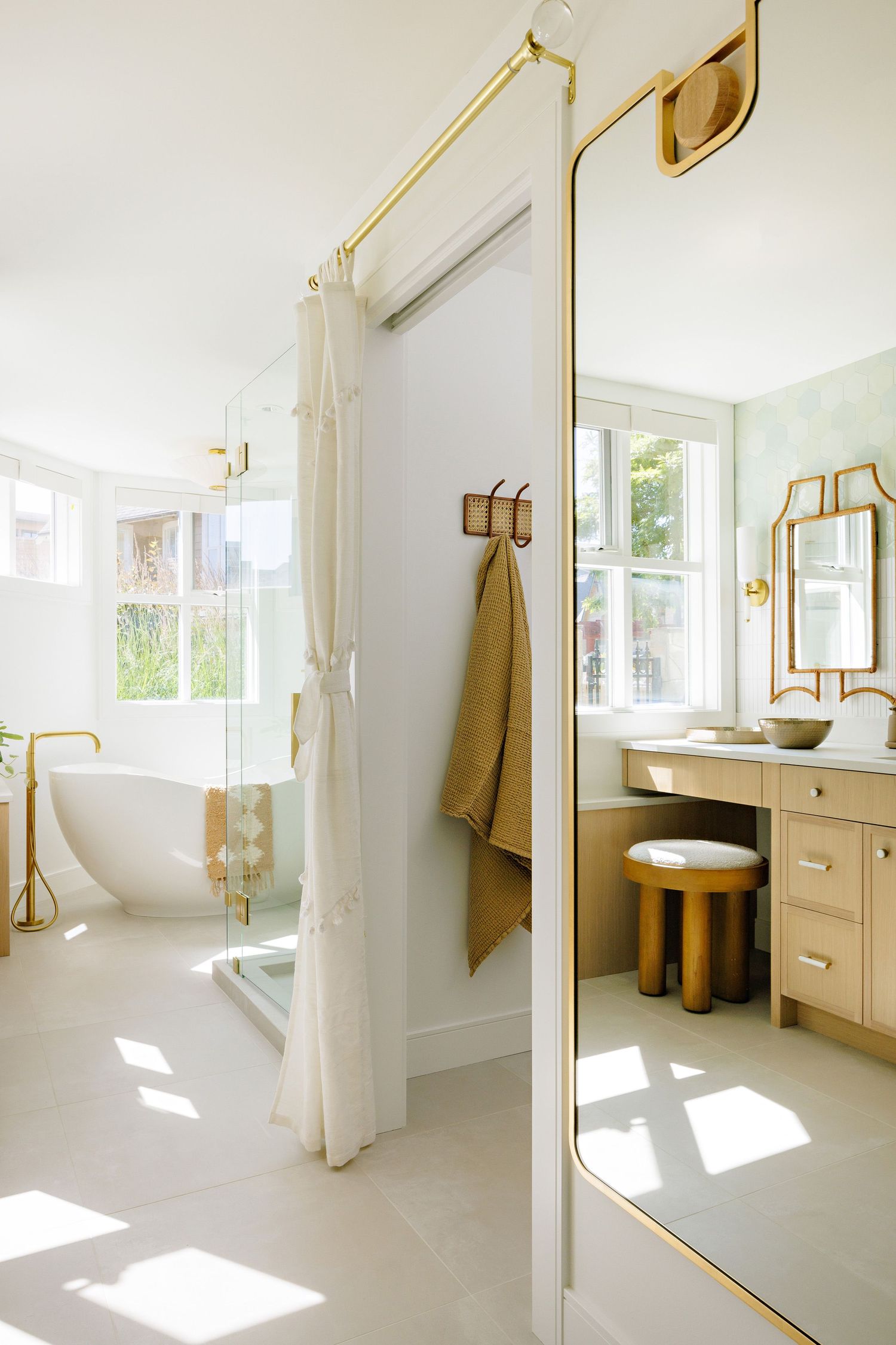 Sunlit bathroom interior with freestanding tub, full-length mirror, and natural wood vanity.