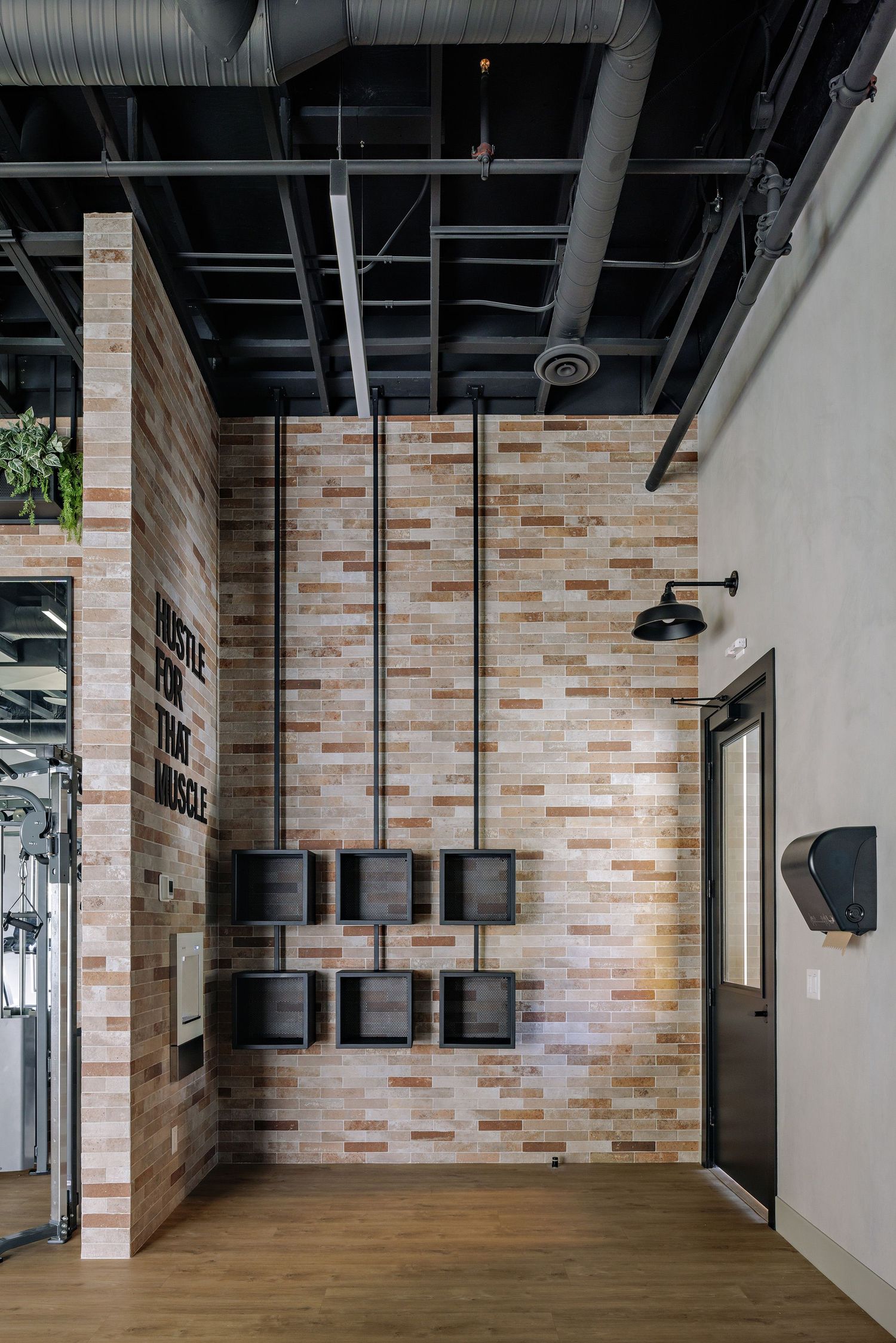 Modern office interior with exposed brick walls, wooden flooring, and industrial black ceiling fixtures.