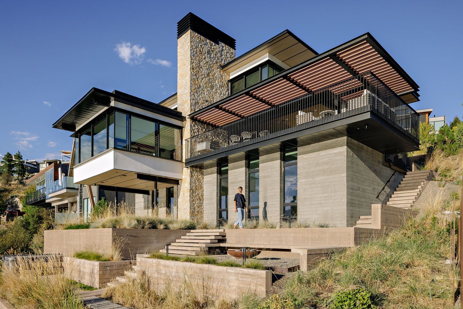 Modern hillside luxury home with stone facade, wood accents, and large windows overlooking scenic landscape.