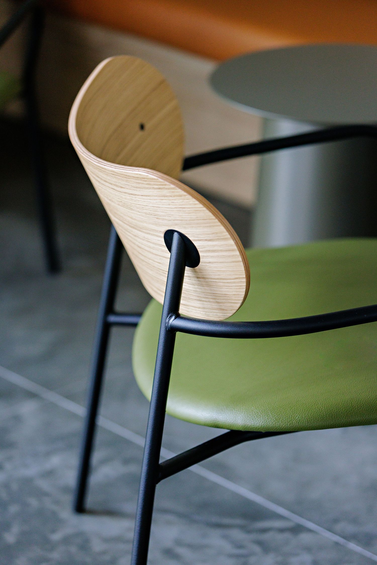 Close-up of a modern dining chair with curved wooden backrest, black metal frame, and olive green cushioned seat.