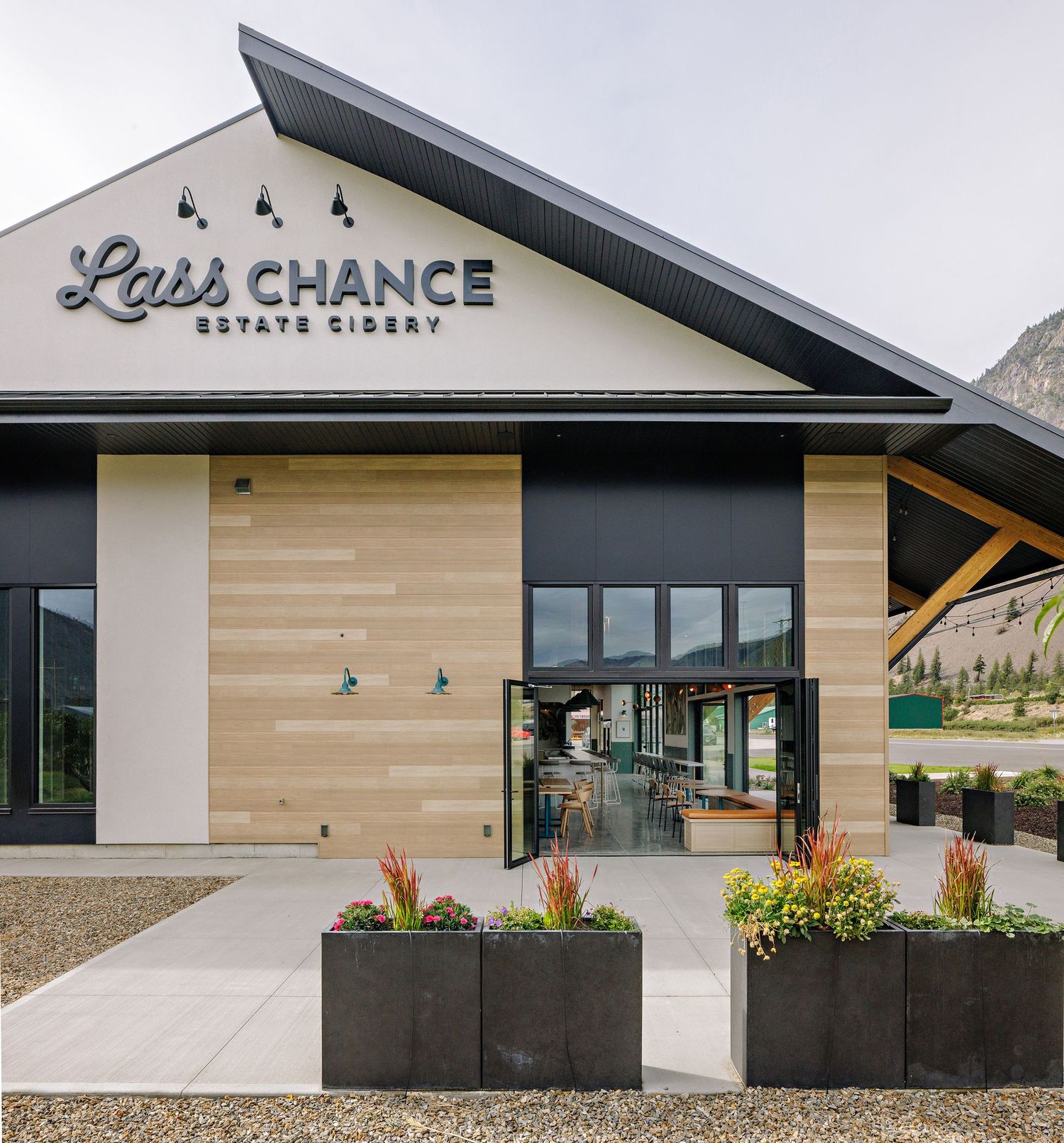 Modern black and wood exterior of Last Chance Estate Cidery with planters and mountain backdrop.