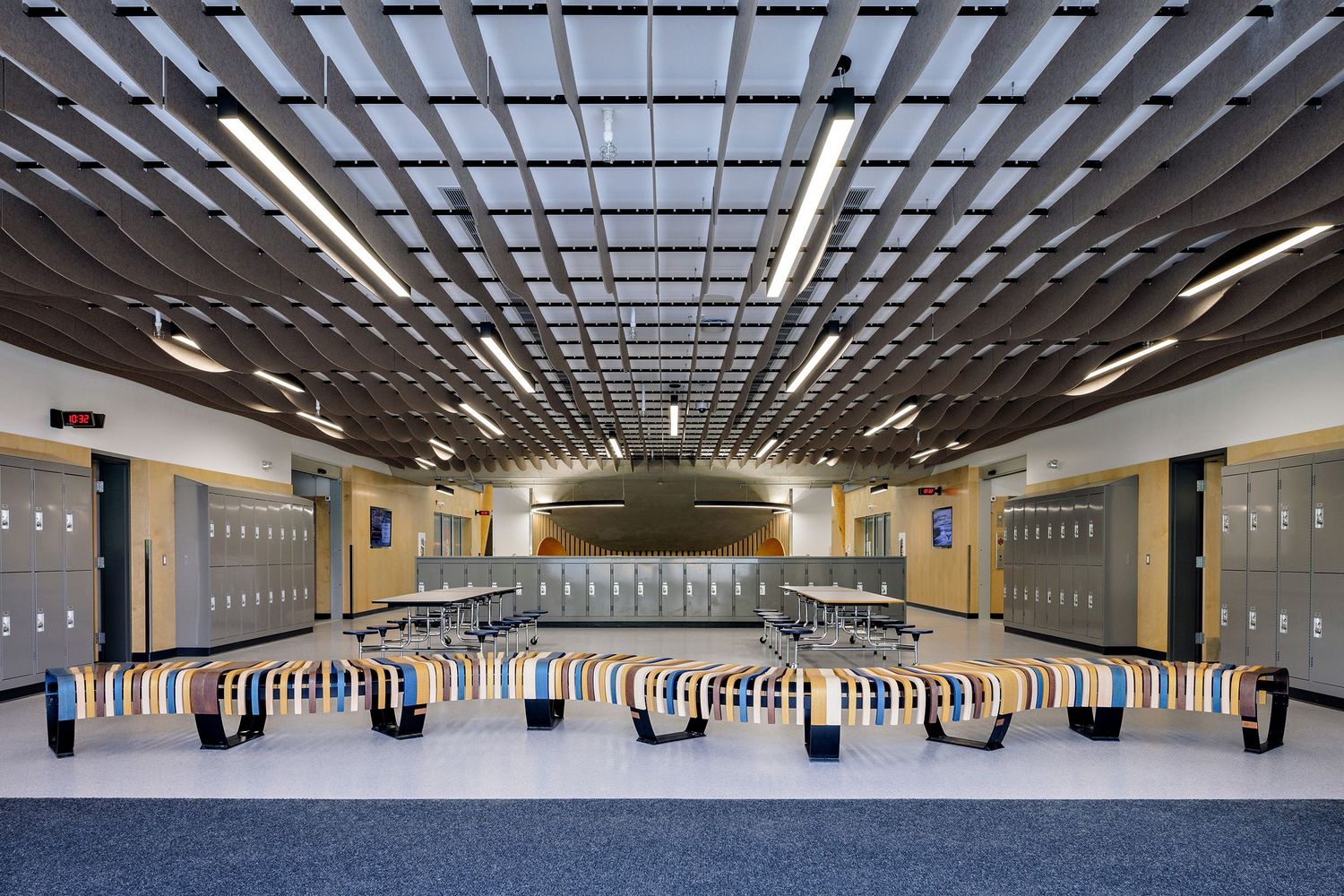 Large music rehearsal room with tiered seating platforms and gray lockers along the yellow walls.