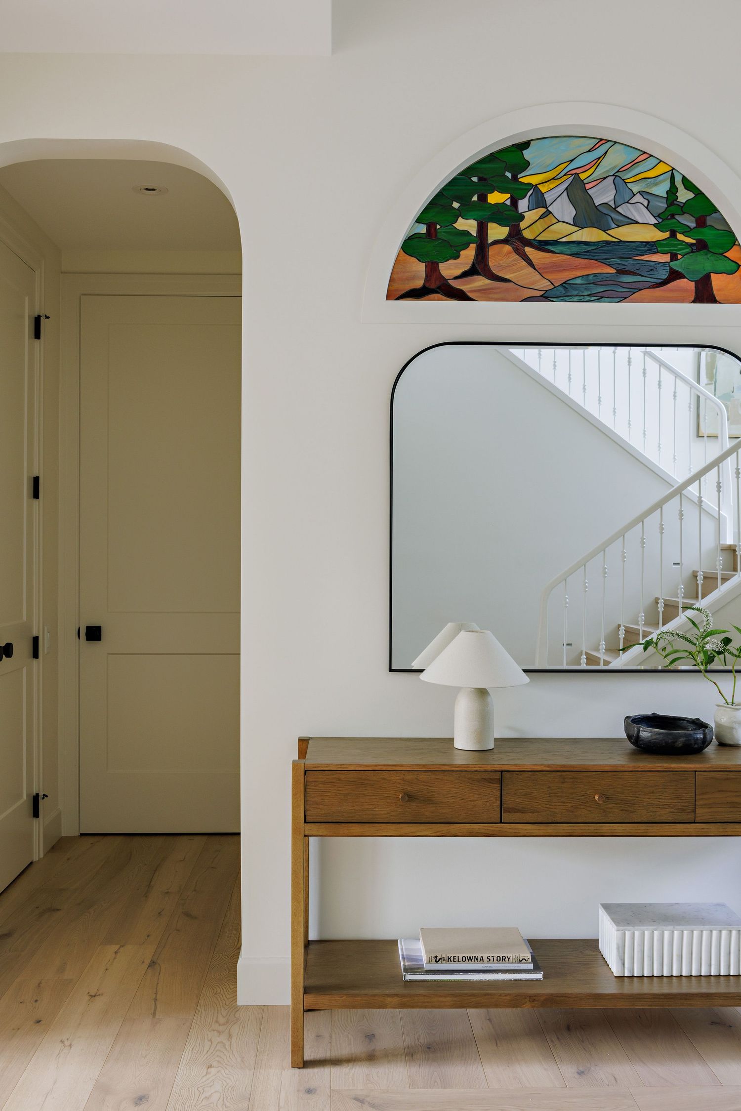 Entryway featuring a wooden console table, stained glass arch window, and white walls with natural light.