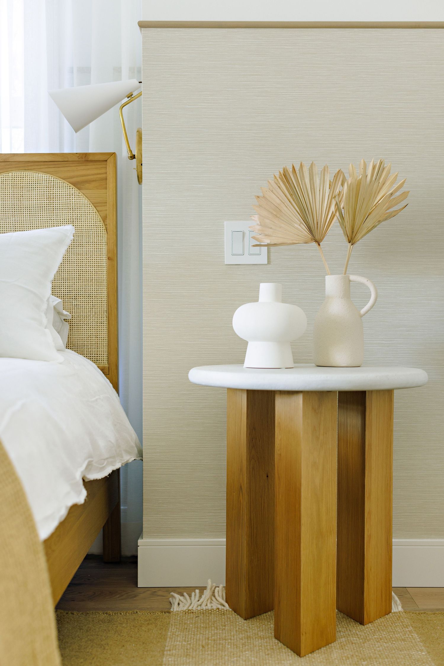 Modern bedroom side table with white marble top and wooden base displaying minimalist white vases.
