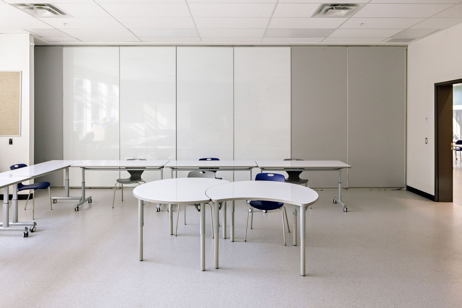 Modern classroom interior with white curved tables arranged in a semi-circle and minimalist white walls.