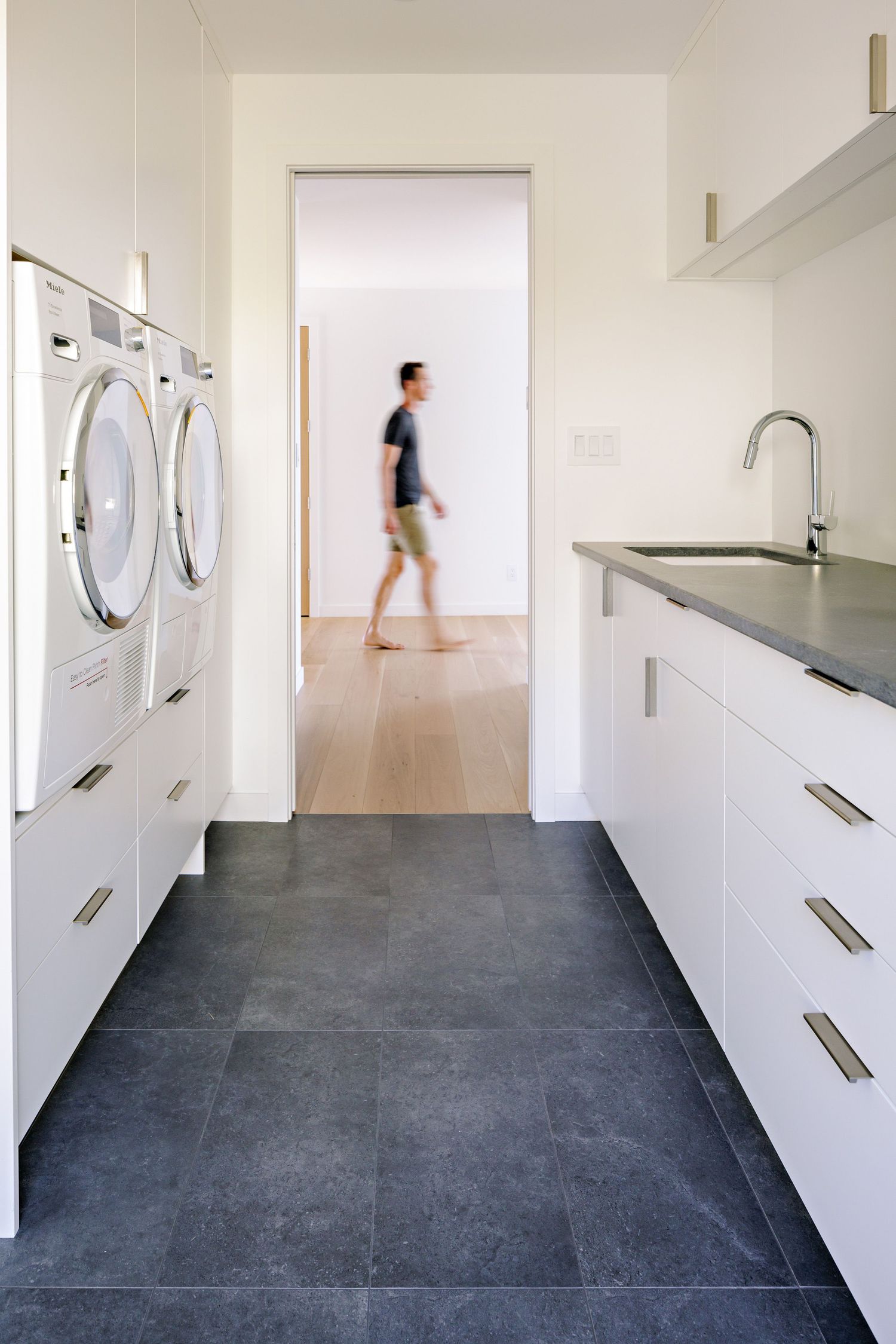 White laundry room with stacked washers, gray tile flooring, and built-in cabinets along one wall.