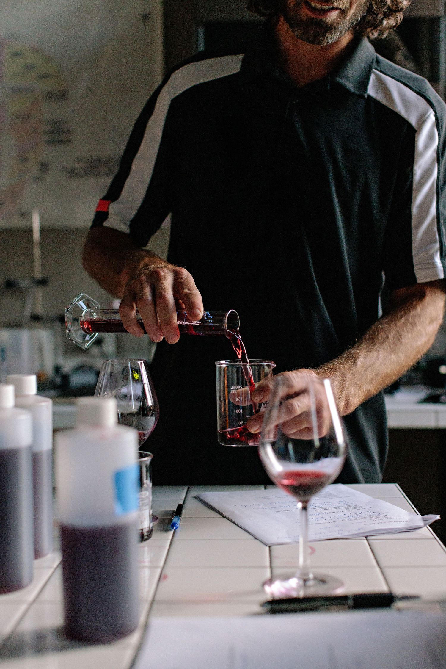 Someone in a striped polo shirt carefully pours red wine into a glass during a wine tasting service.