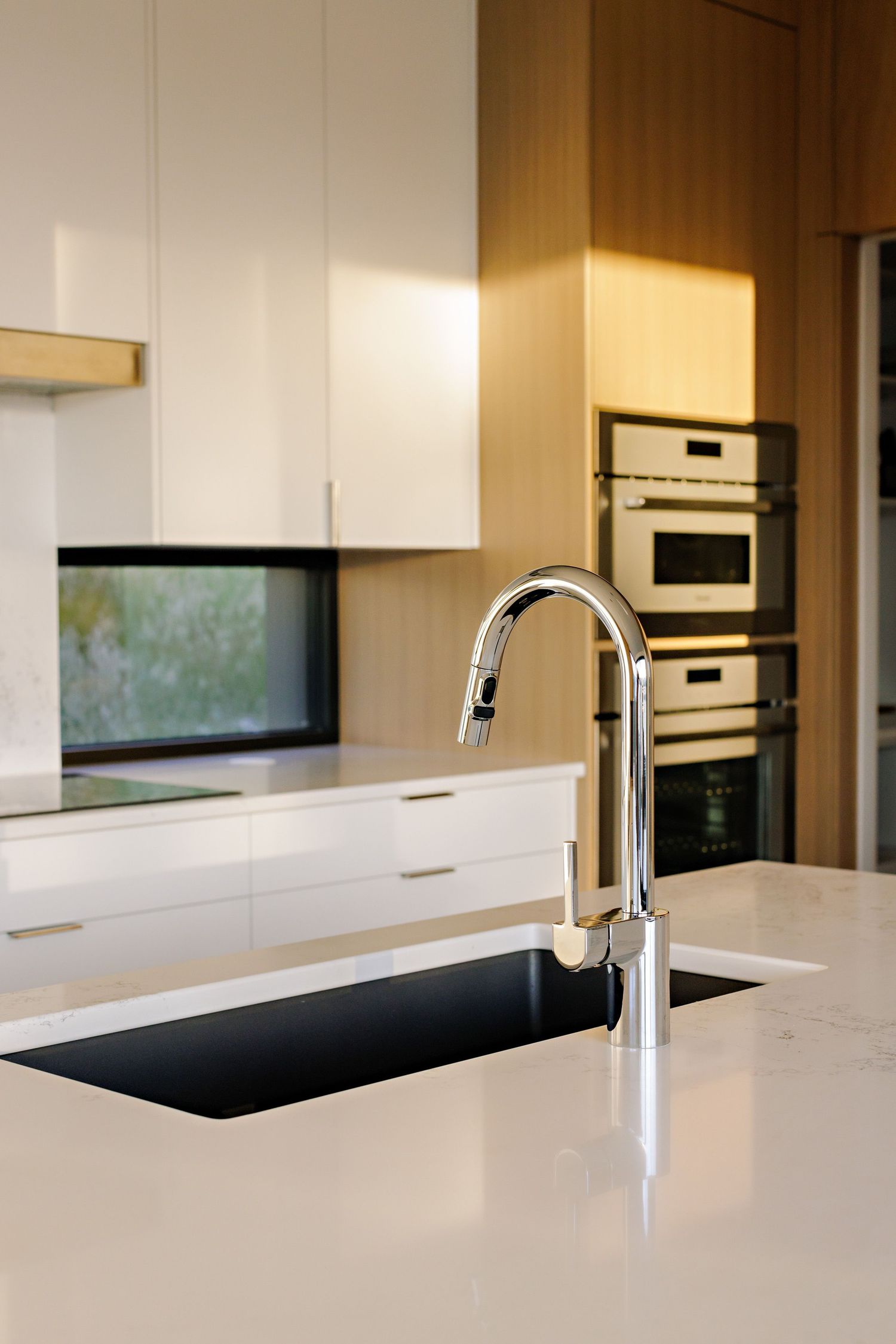 Contemporary white kitchen featuring a sleek chrome faucet, black undermount sink, and built-in wall appliances.