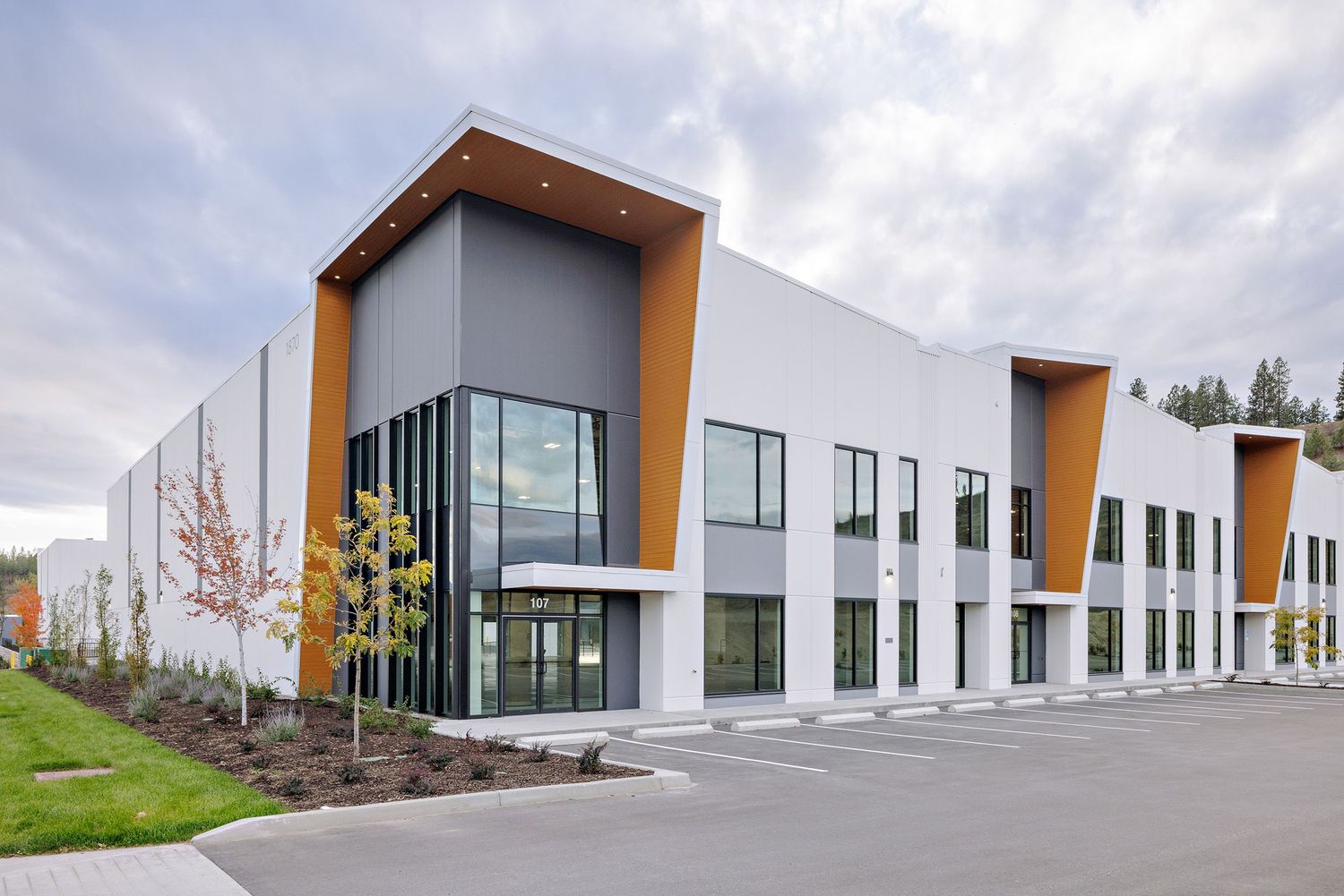 Modern industrial office building exterior with white walls, orange accents and glass windows in suburban setting.