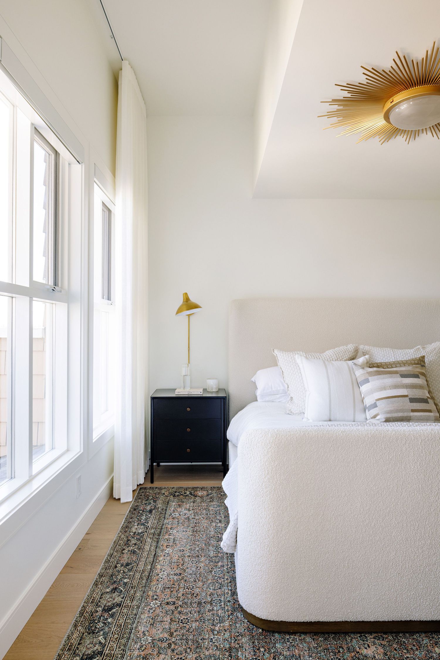 Minimalist bedroom with white bedding, vintage rug, and sunburst ceiling light fixture.
