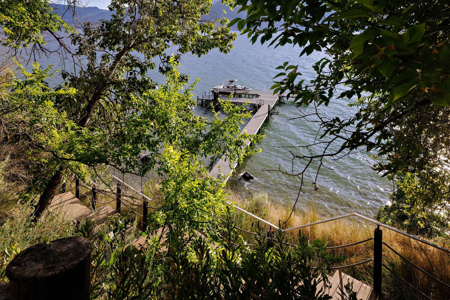 A wooden dock extends into a scenic lake surrounded by lush greenery and mountains in the background.