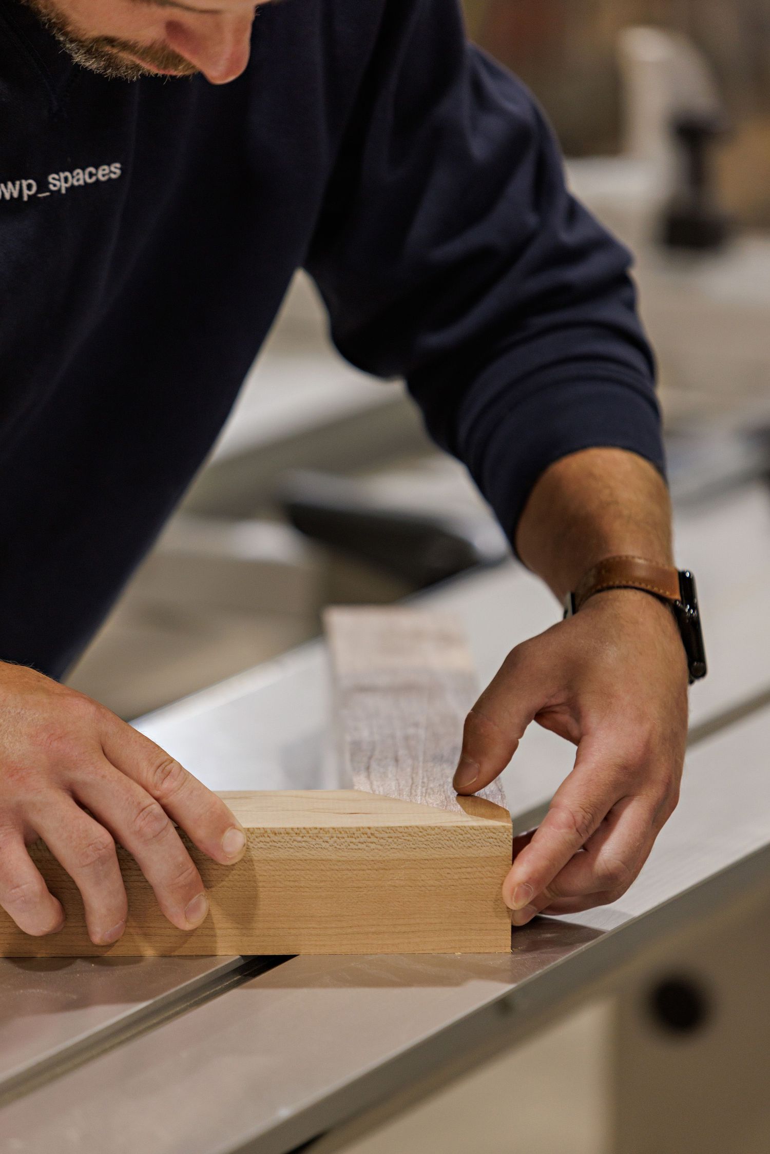 Hands guiding a wooden plank through a table saw for precise cutting in a woodworking workshop.