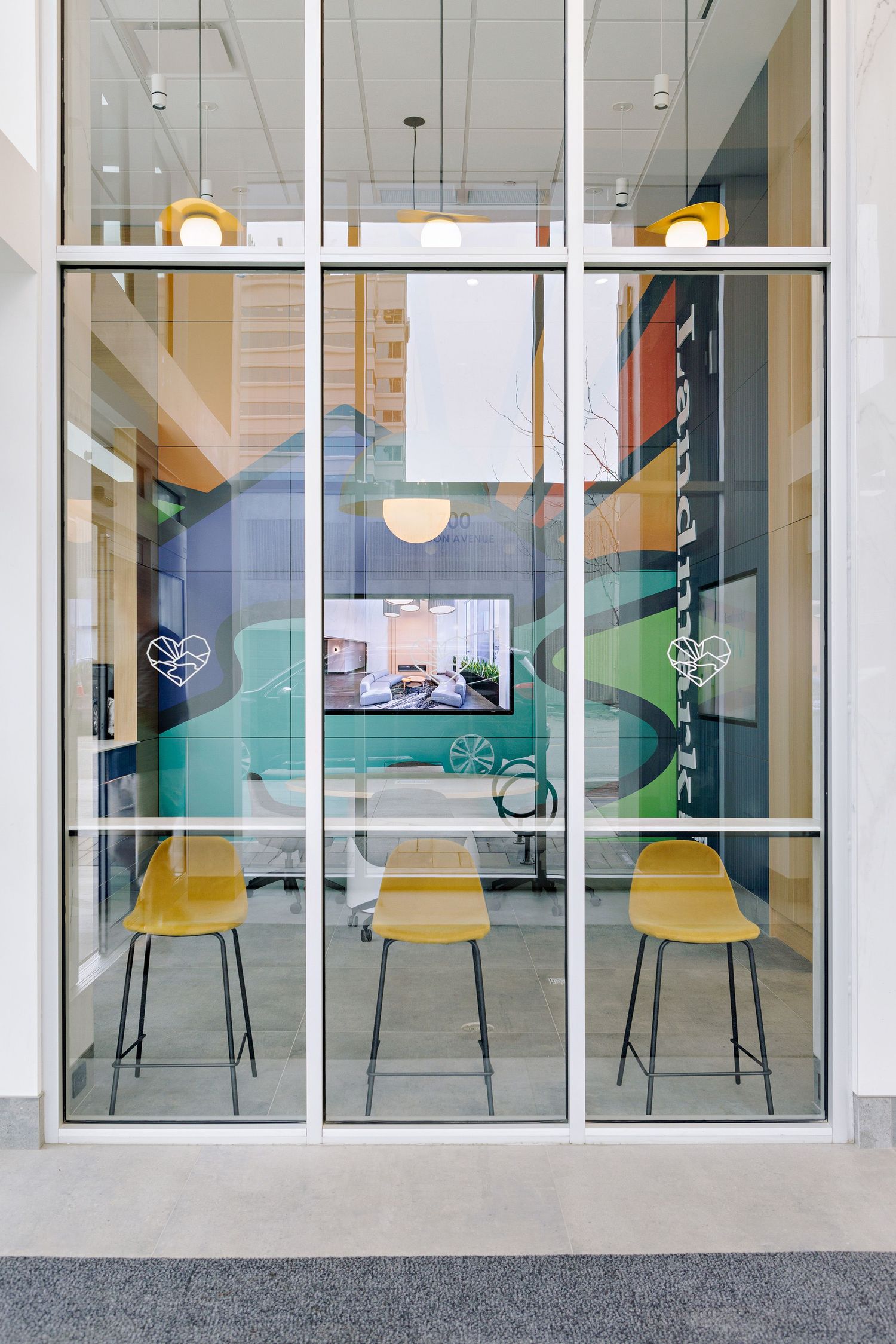 Modern office meeting space with three yellow chairs behind glass panels featuring green accent walls and pendant lighting.