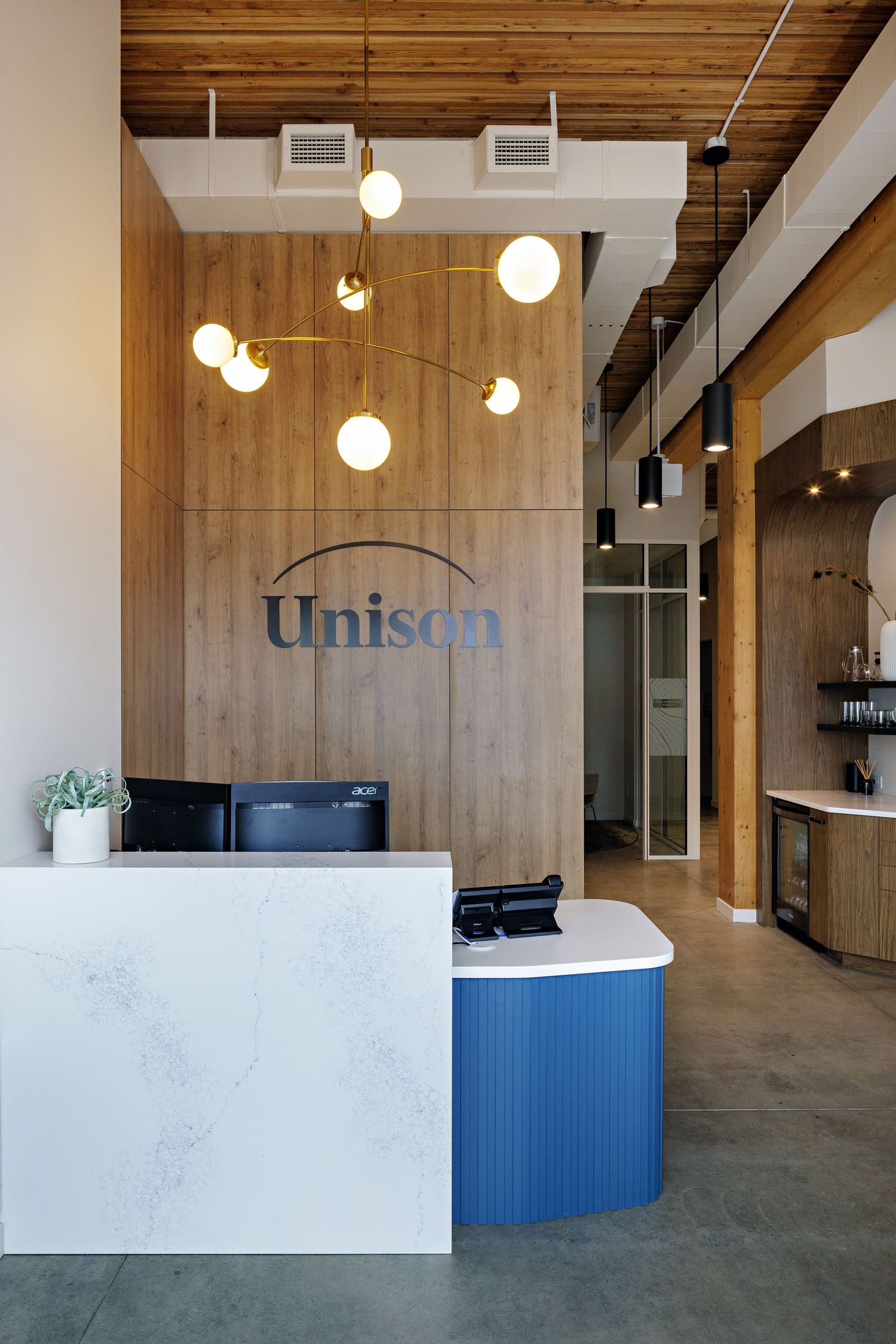 Modern office reception area with wood paneling, marble counter, blue accents, and hanging globe pendant lights.