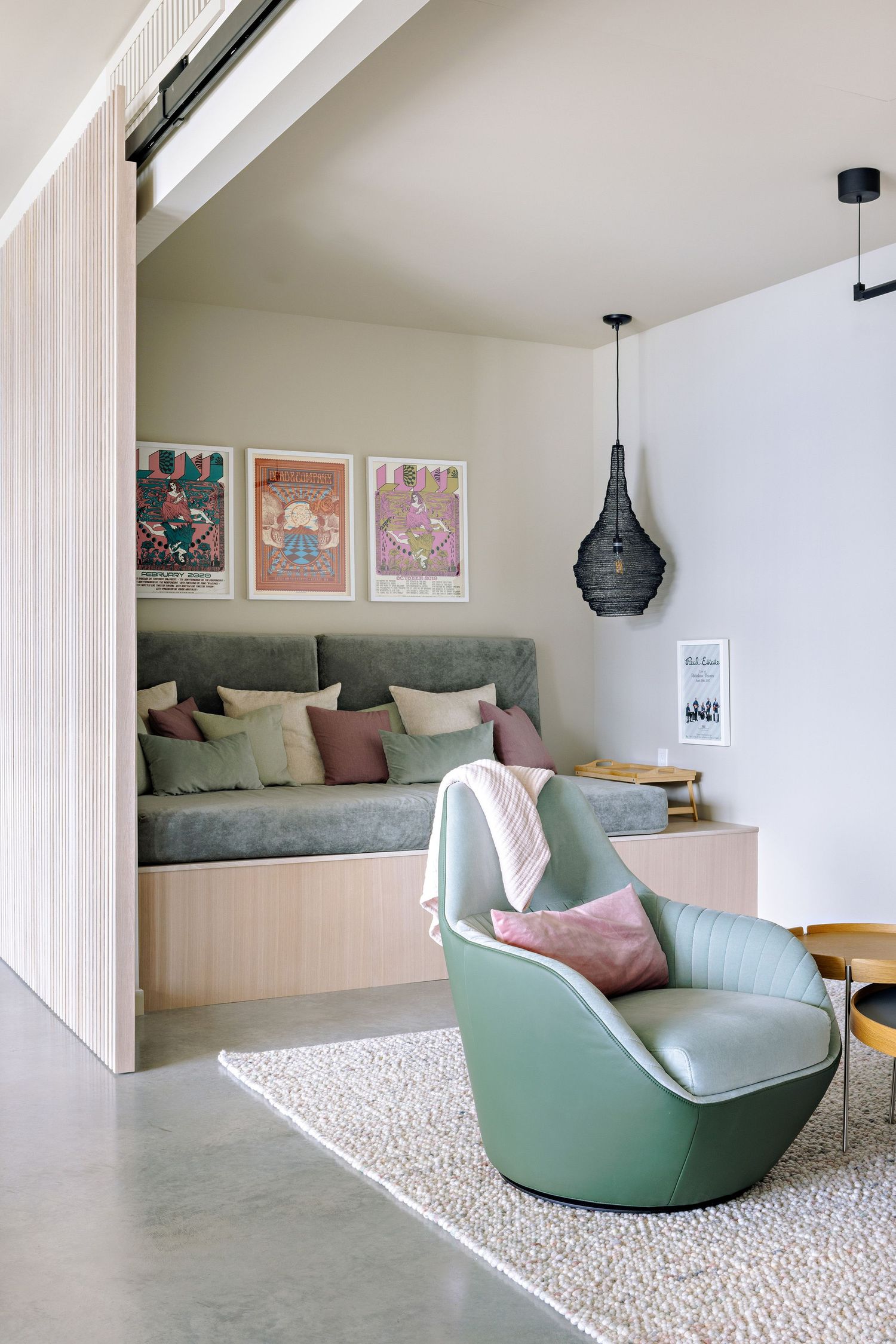 Modern reading nook features a built-in bench with sage cushions, retro mint chair, pendant light, and vintage art prints.