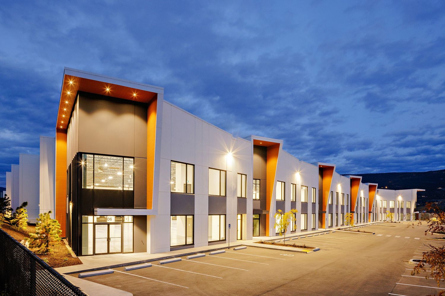 Modern two-story townhomes with illuminated exteriors at dusk showcase contemporary architectural design against a blue sky.