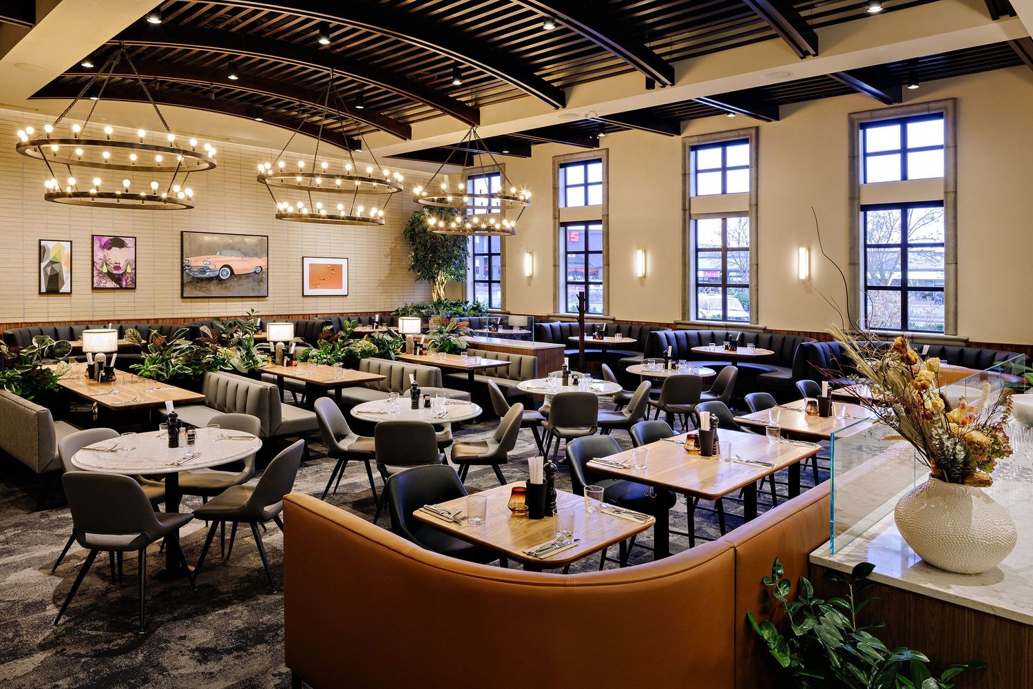 Elegant restaurant dining room with high ceilings, chandeliers, leather booths, and large windows providing natural light.