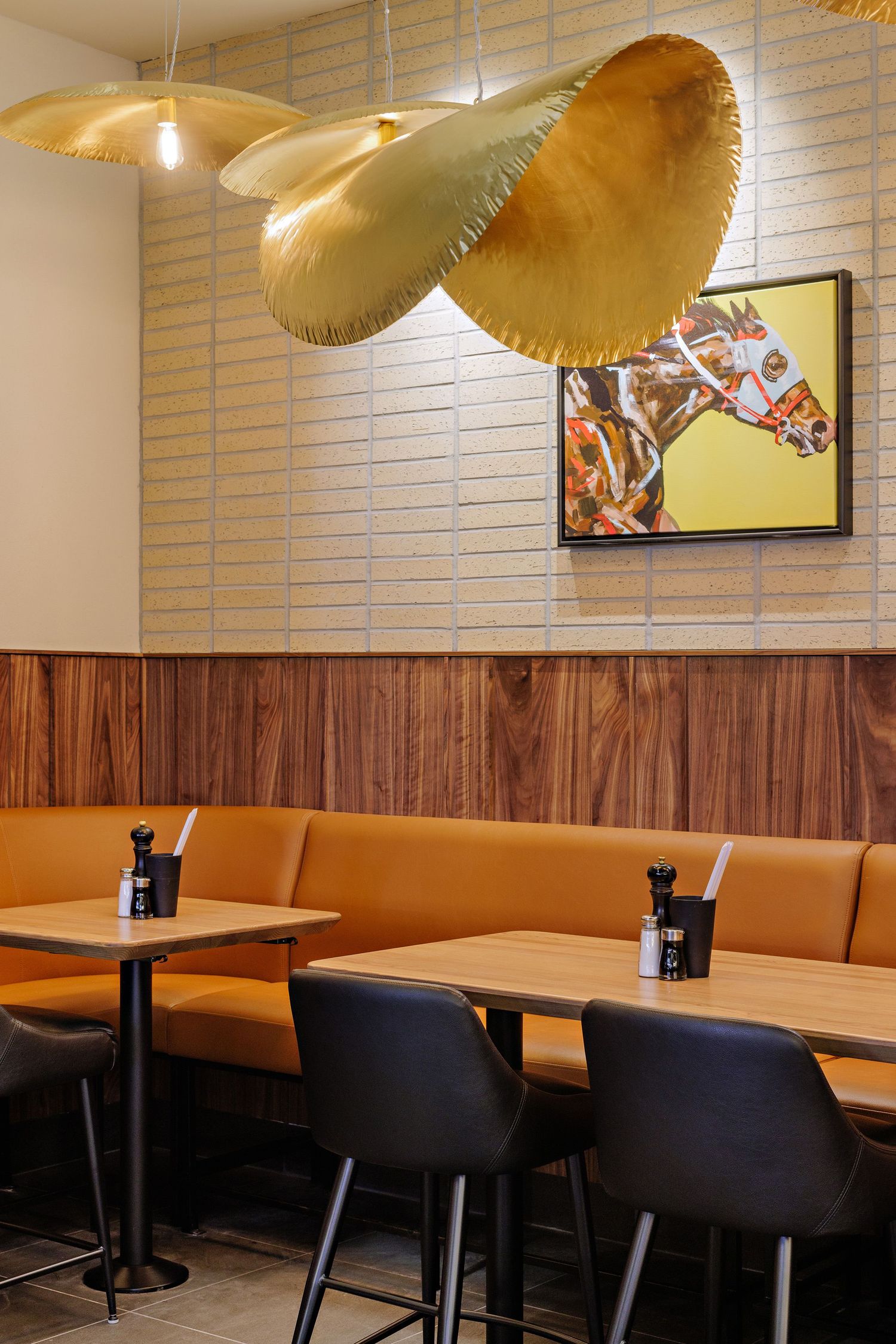 Modern restaurant interior with orange booth seating, pendant mushroom lamps, and horse artwork on wood-paneled walls.