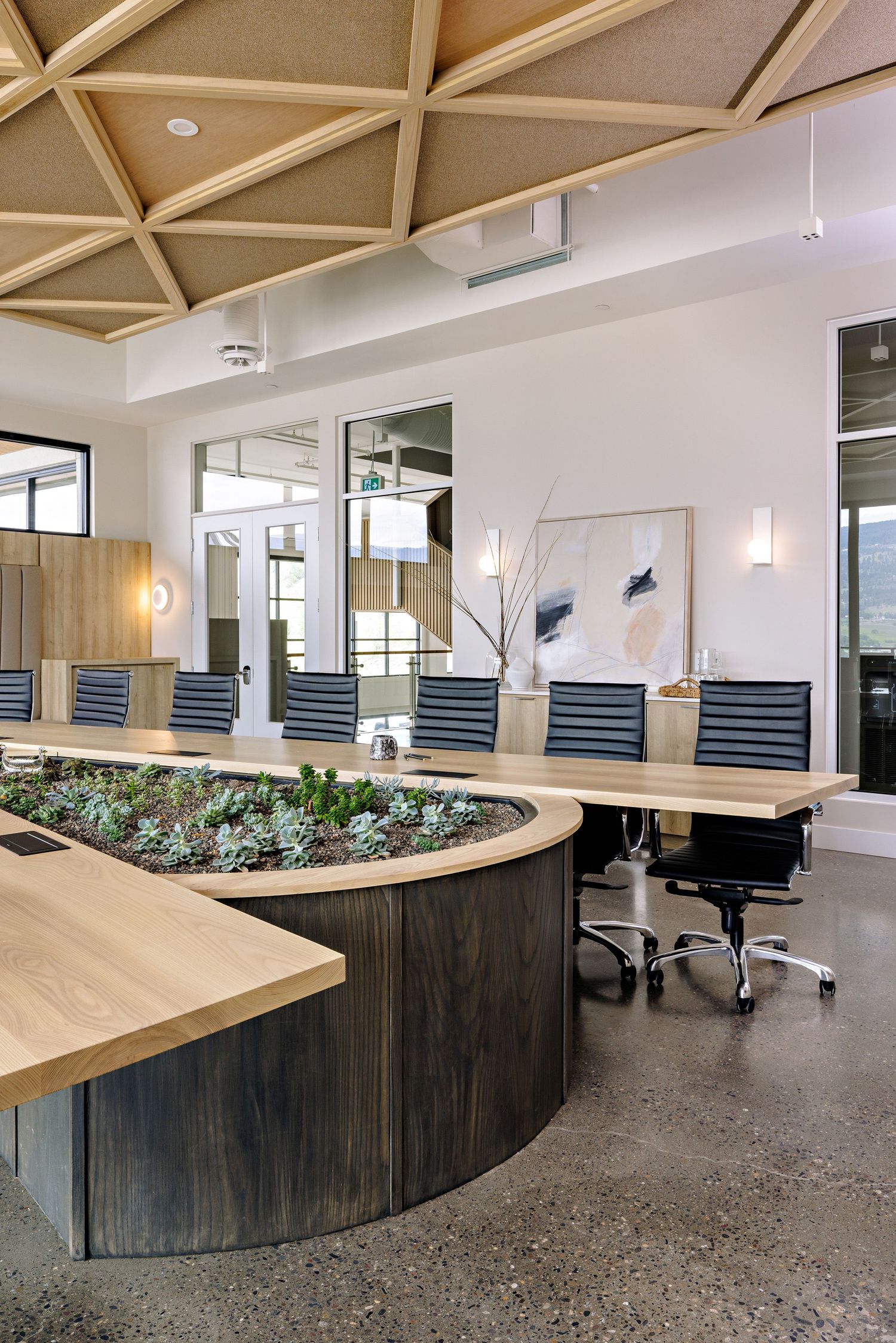 Modern office meeting space with geometric ceiling, blue chairs, and a curved wooden planter integrated into the conference table.