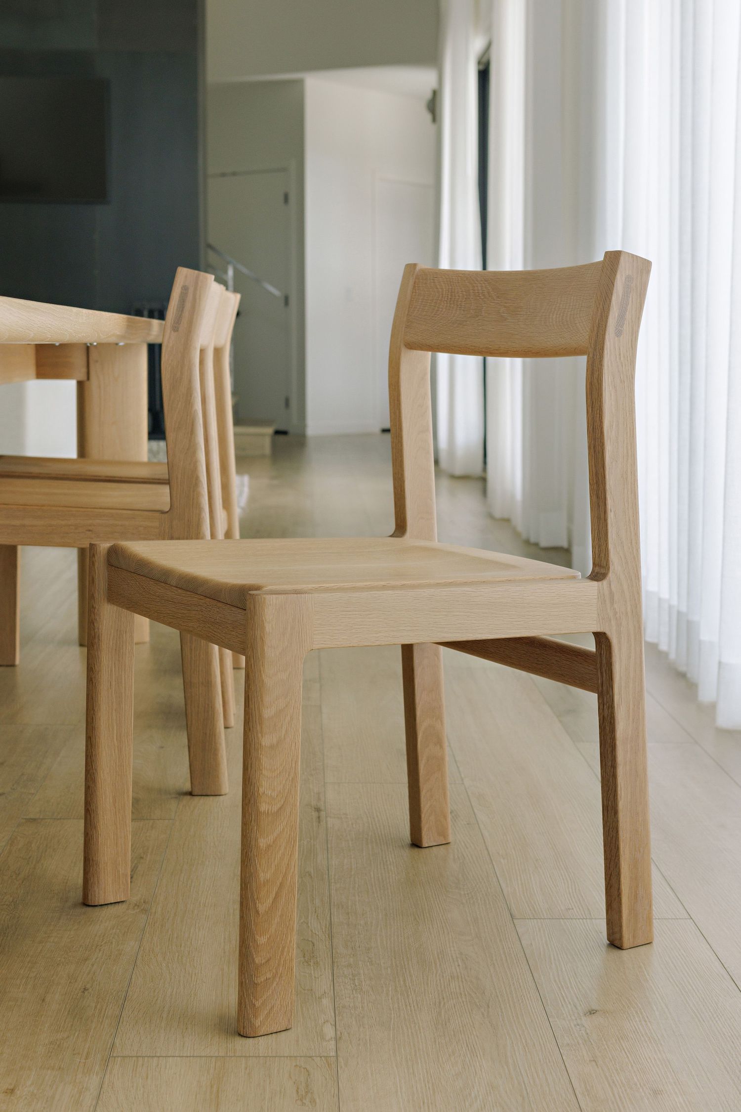 Minimalist wooden chair design shown from multiple angles on light wood flooring in a bright interior space.
