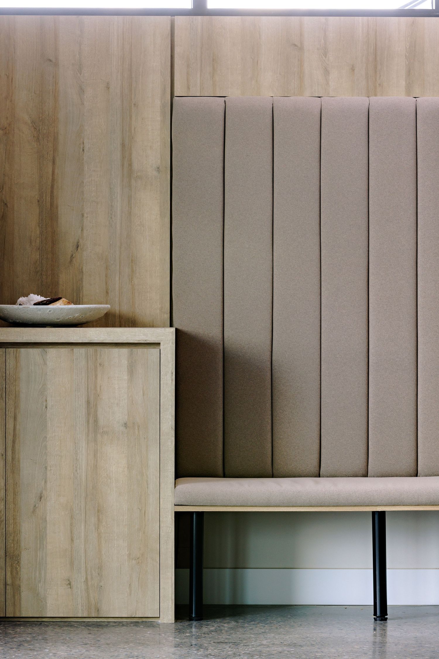 Modern minimalist bench seating with light wood paneling and white vertical slats creates a sleek waiting area interior.