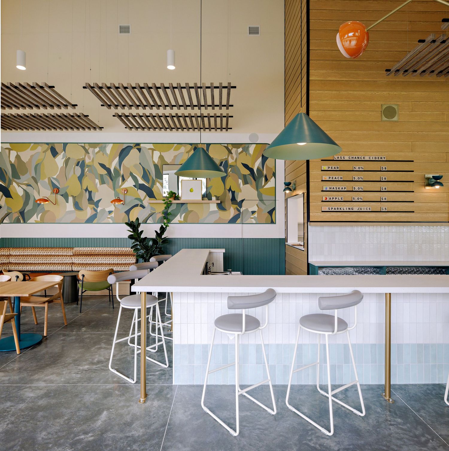 Modern cafe interior with white bar stools, turquoise pendant lamp, and floral wallpaper against wooden wall paneling.