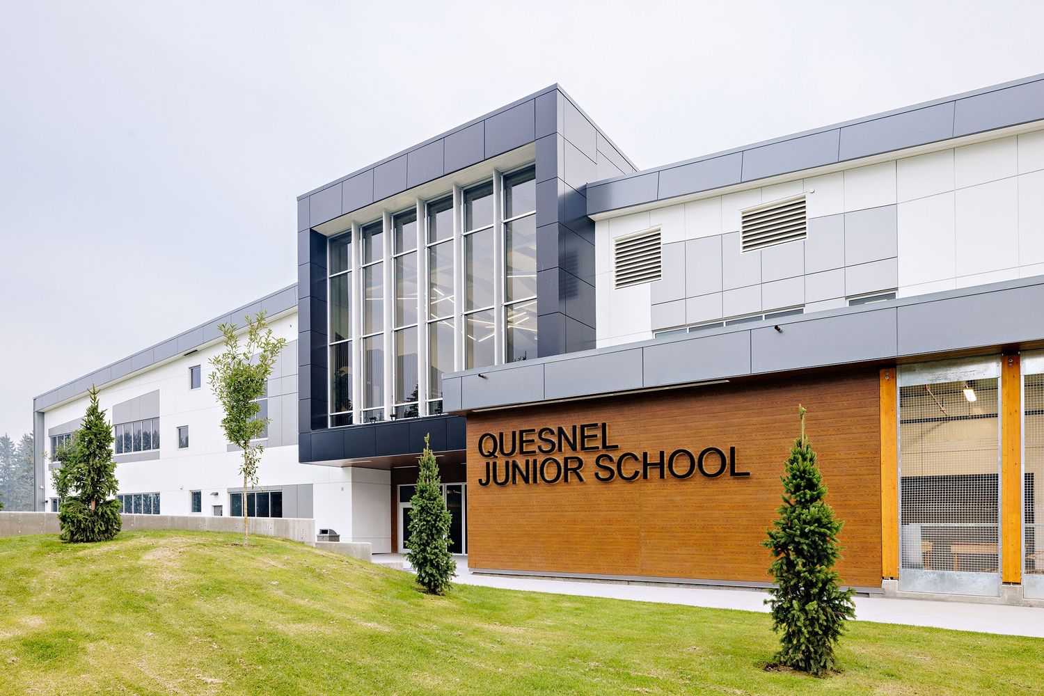 Modern exterior of Quesnel Junior School featuring contemporary architecture with glass panels and wooden signage.