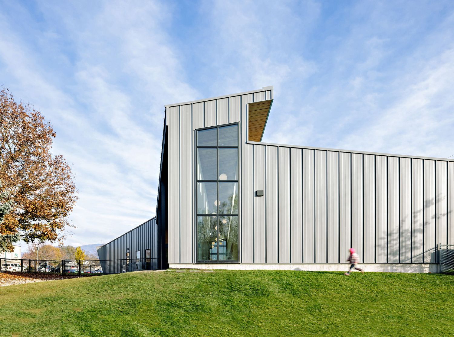 Modern white architectural building with glass panels and grassy hill shown in multiple angles against blue sky.