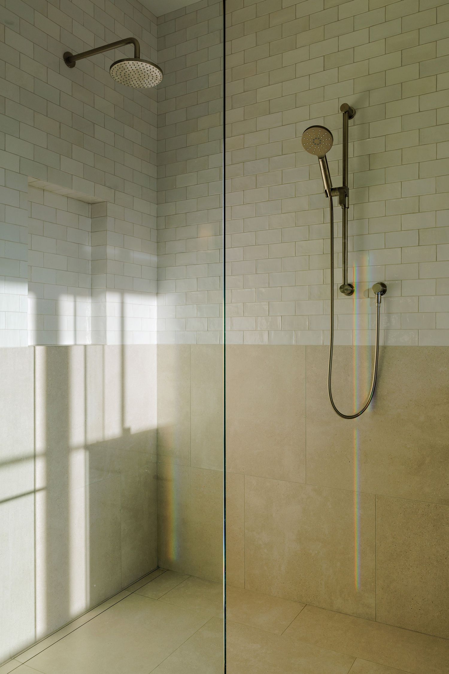 Modern glass-enclosed shower with white subway tile walls and brass fixtures in a bright bathroom.