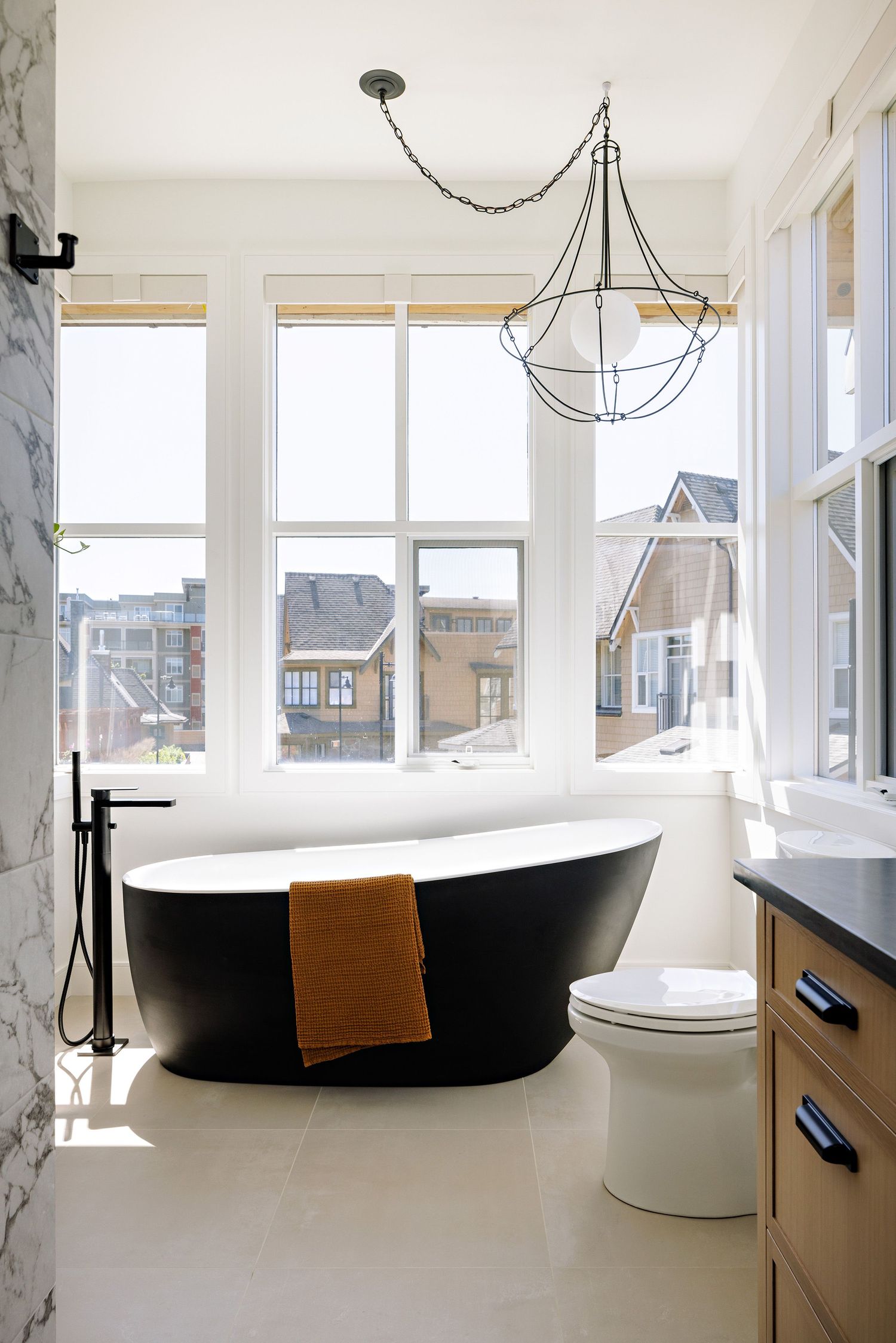 Luxurious bathroom with freestanding black tub, chandelier, and large windows overlooking city views.