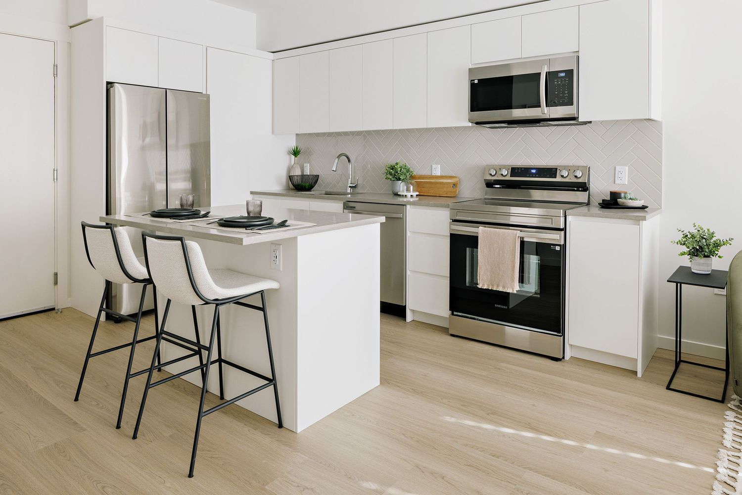 Contemporary white kitchen featuring stainless steel appliances, breakfast bar, and light wood flooring.