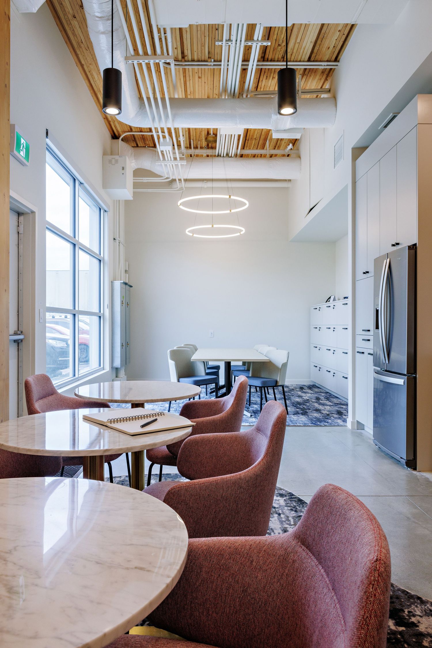 Modern office breakroom with circular pendant lights, rust-colored chairs, and wooden ceiling panels.