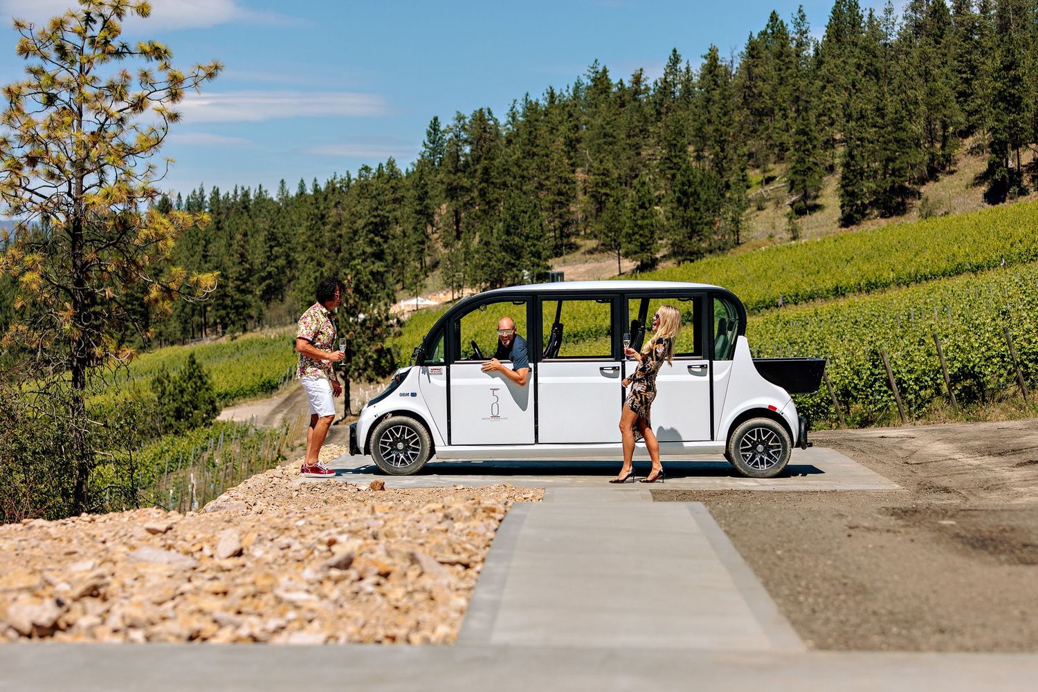 Autonomous electric shuttle parked on hillside road surrounded by green forest and mountain landscape in summer.