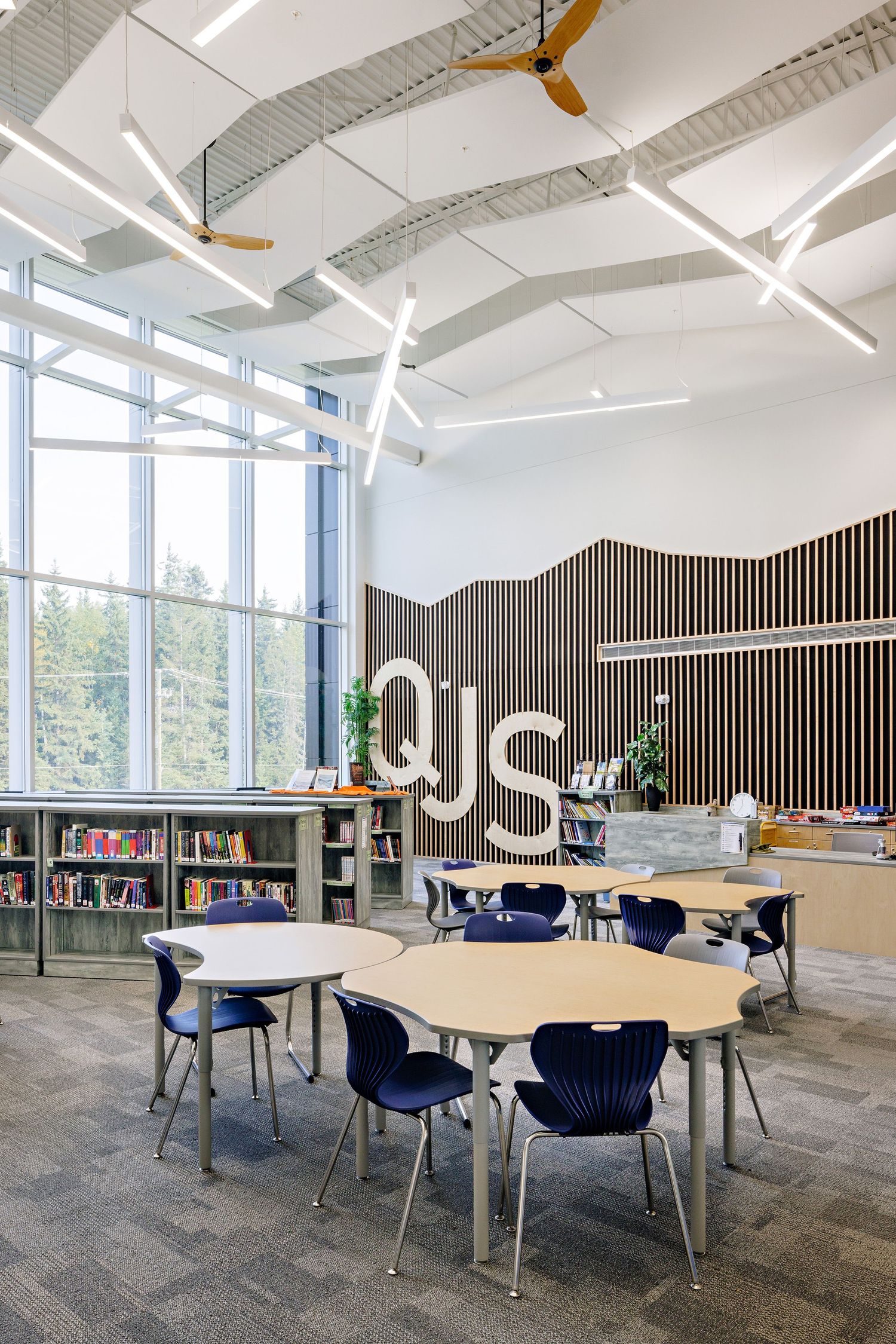 Modern educational space with round tables, blue chairs, bookshelves, and contemporary architectural elements with natural lighting.