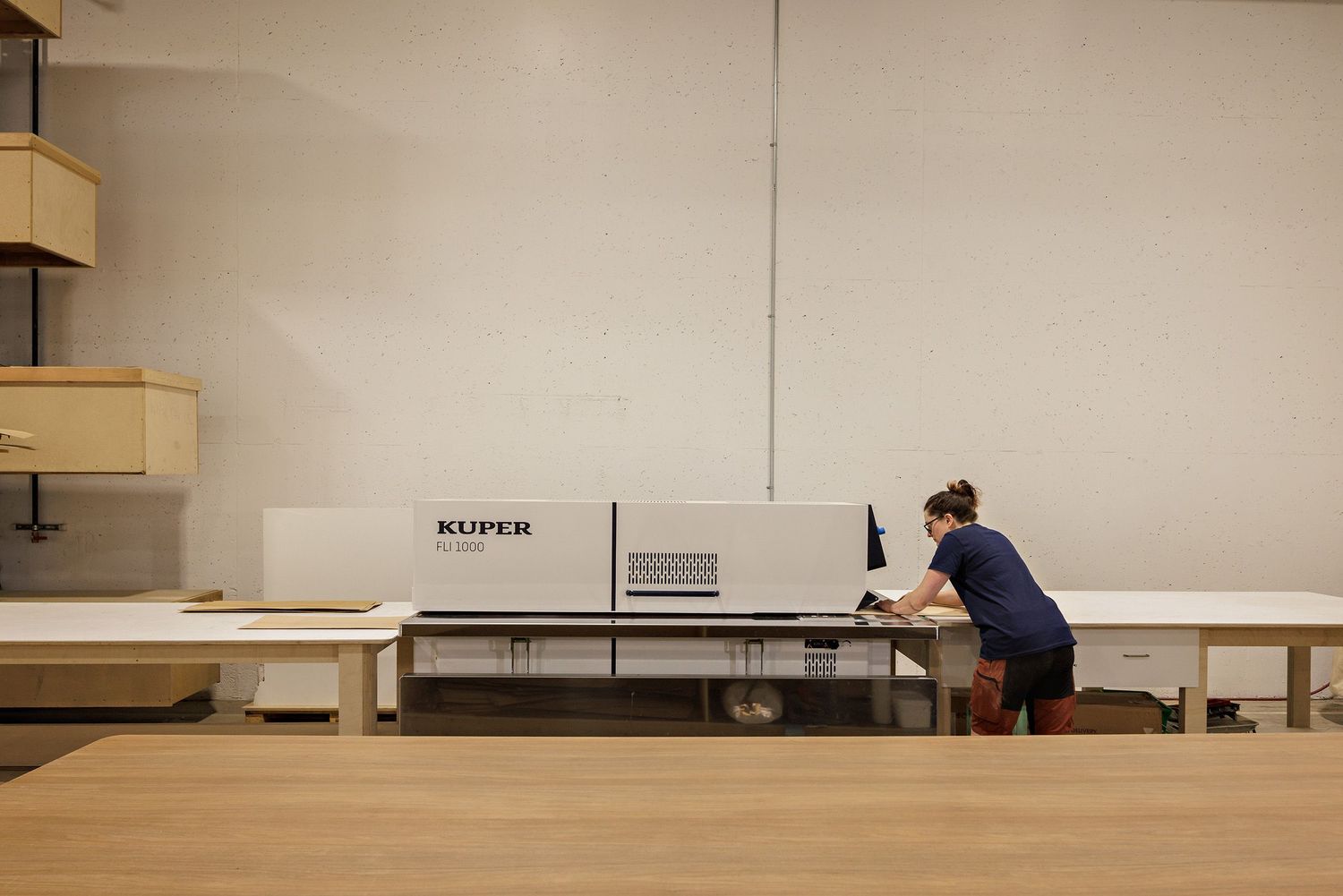 Person working at large industrial equipment in minimalist workspace with beige walls and wooden surfaces.