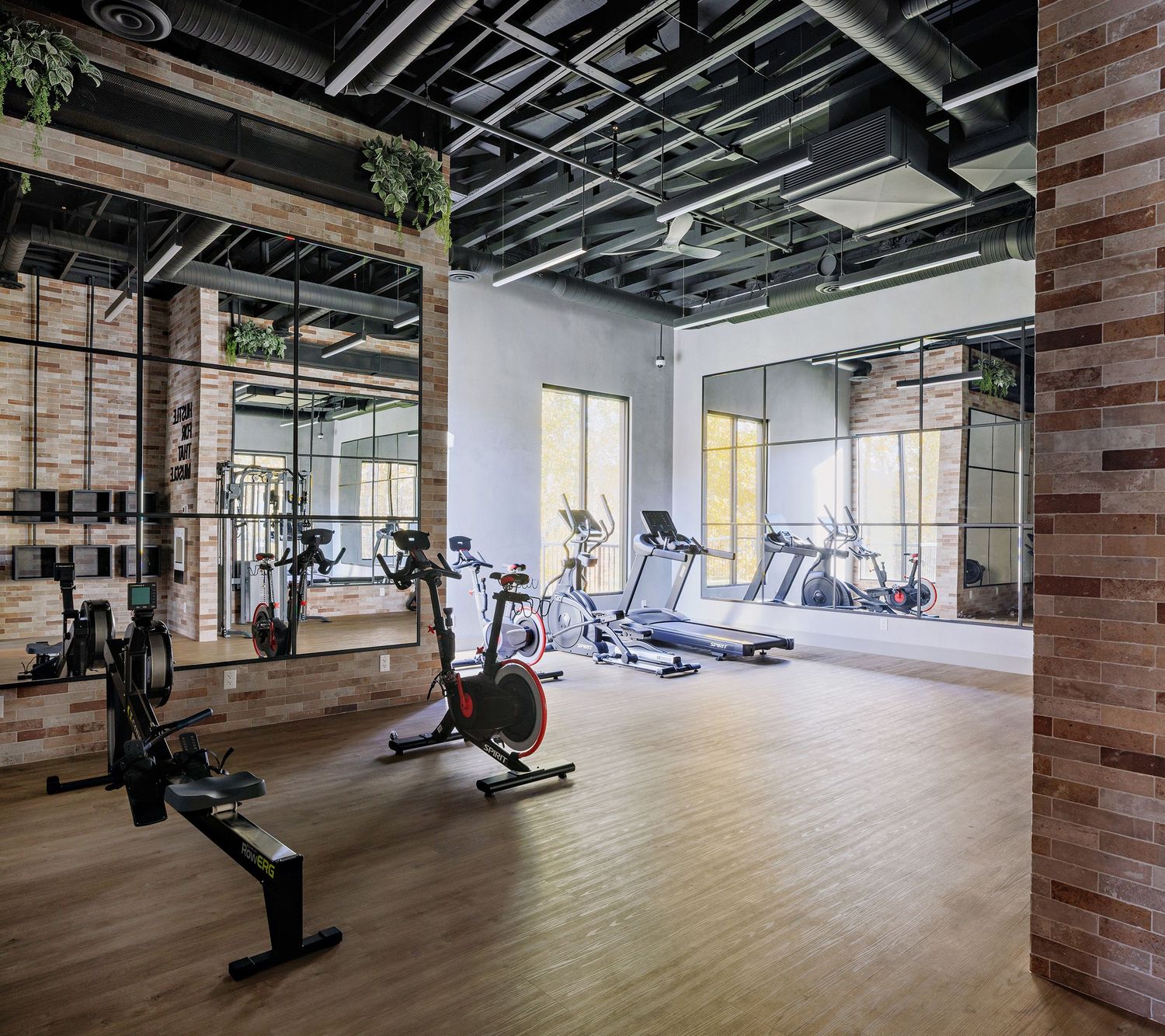 Modern fitness center interior with wooden floors, exposed ceiling, and various exercise equipment in an open layout space.