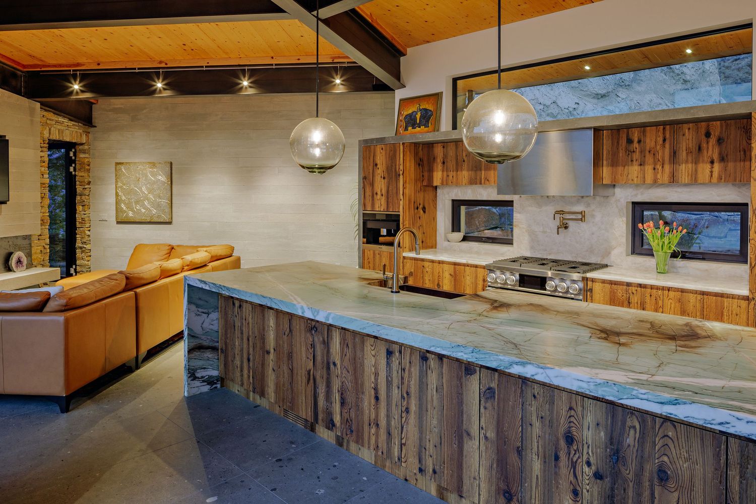 Modern kitchen with reclaimed wood cabinets, concrete countertops, pendant lights and orange leather seating in living area.