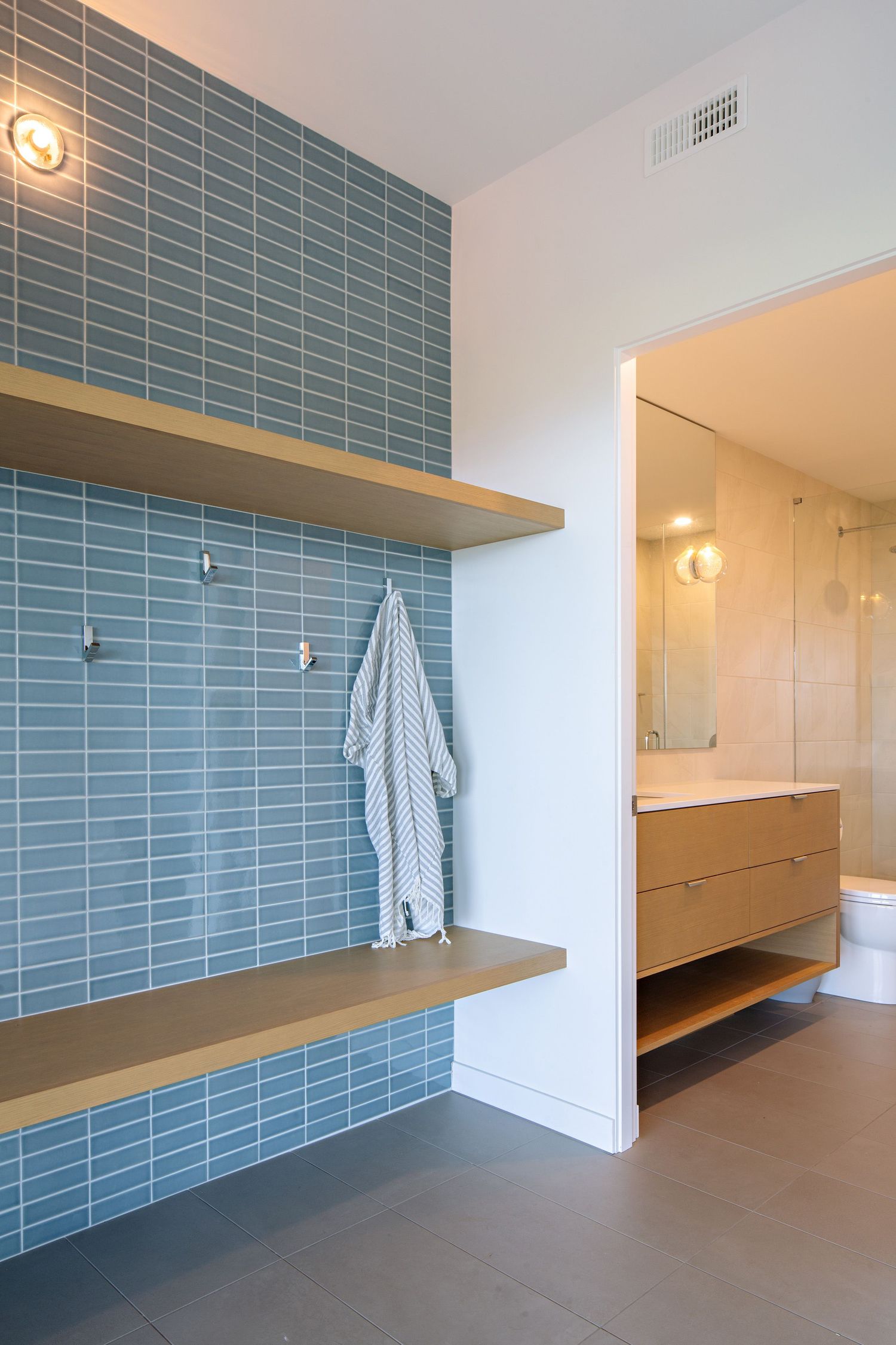 Modern bathroom with blue subway tile wall, floating wooden shelves, and white bath towel hanging in a minimalist design.