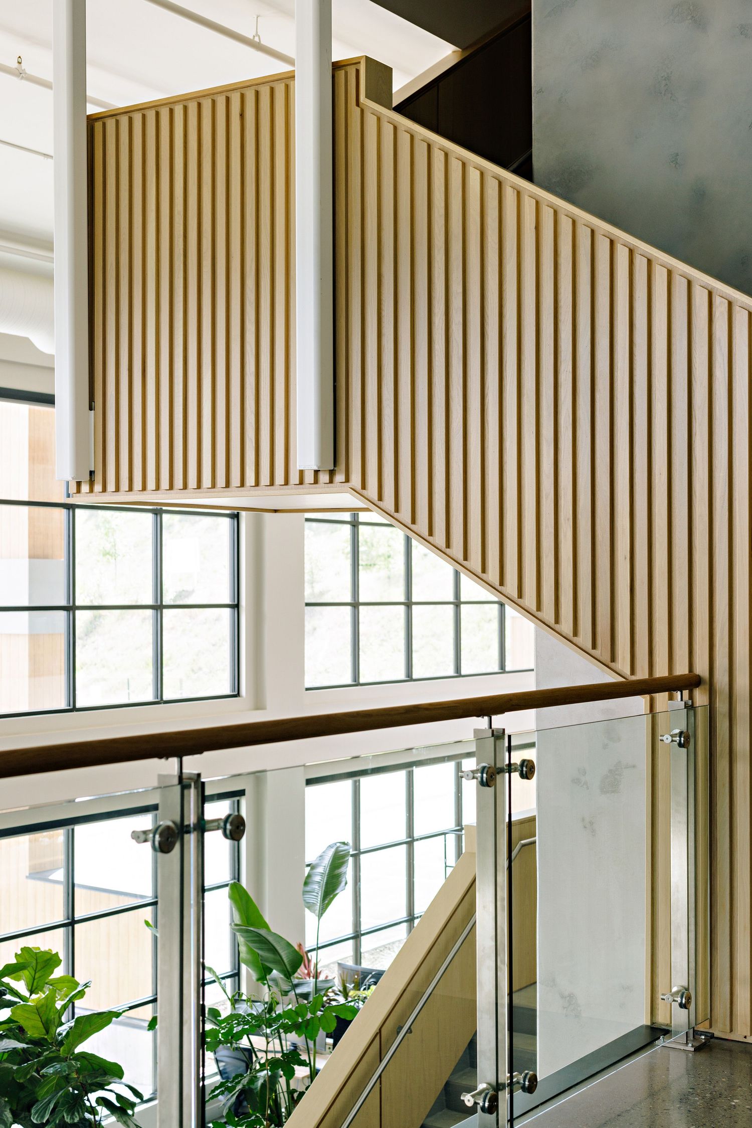 Contemporary staircase with gold vertical slats, glass railing and natural light flowing through large windows.