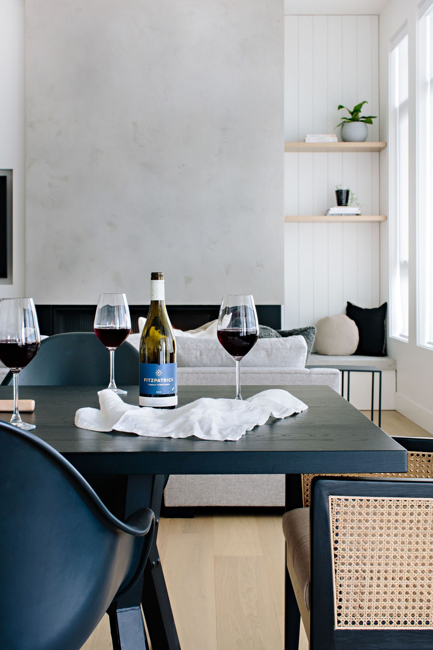 Elegant dining setup with dark blue chairs, wine glasses and wooden shelving against white walls.