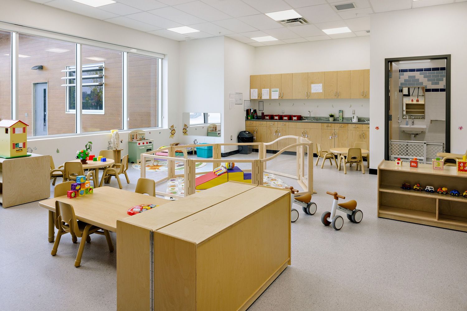 A modern daycare classroom with wooden furniture, toys, and educational materials arranged neatly around the bright space.