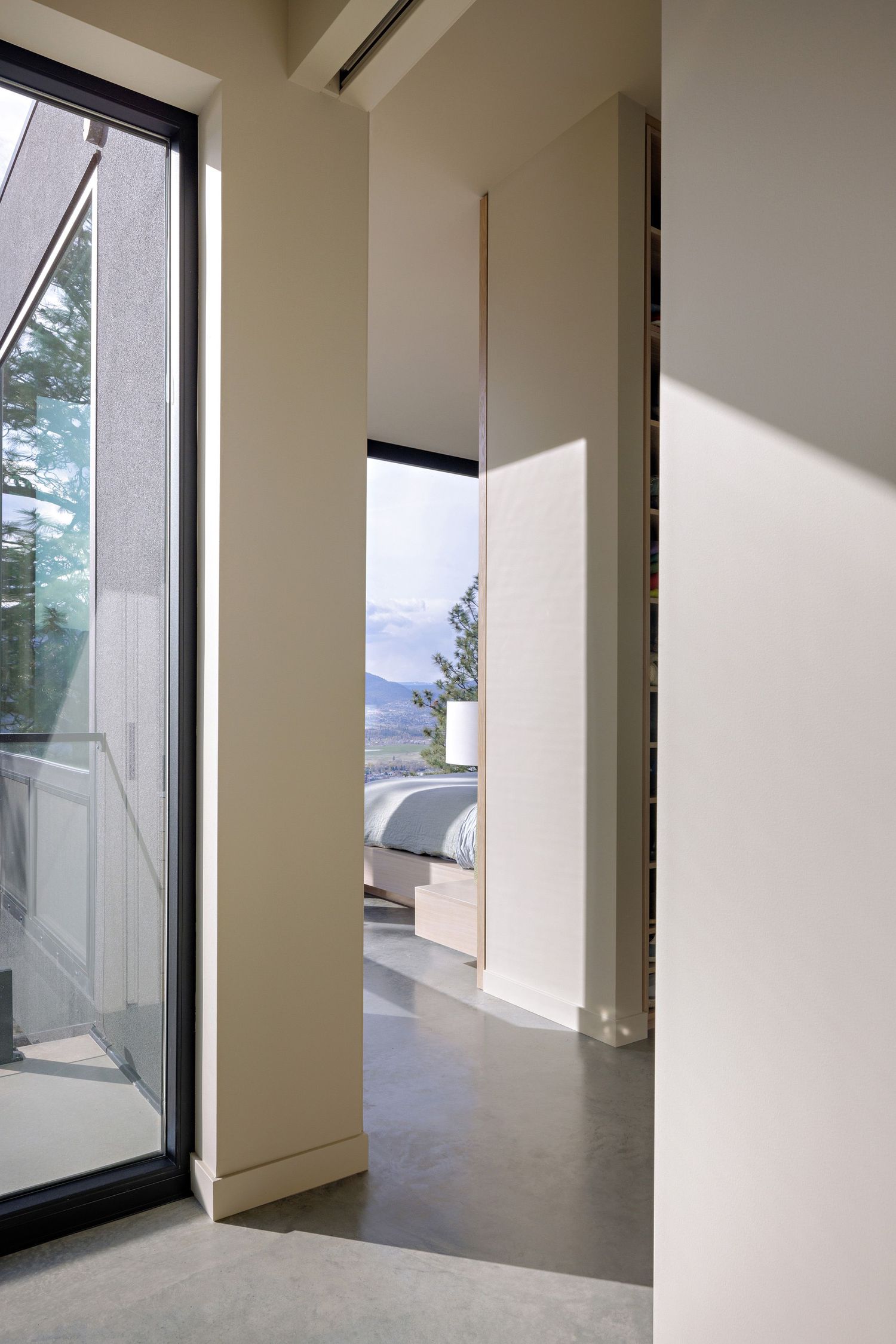 Modern minimalist hallway with polished concrete floors and large windows offering scenic mountain views beyond.
