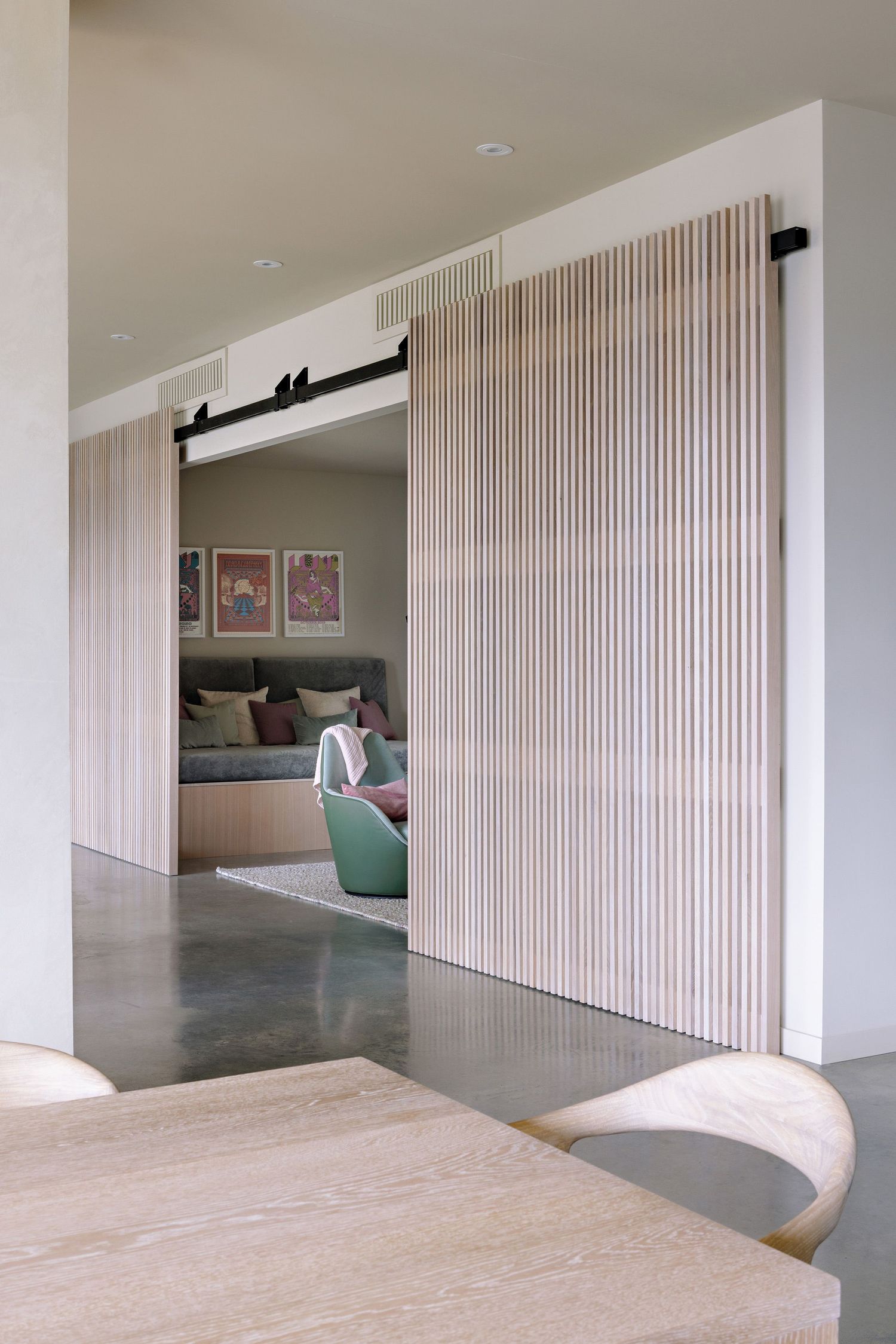 Modern interior with sliding wooden slat barn door revealing a cozy bedroom space with polished concrete floors.