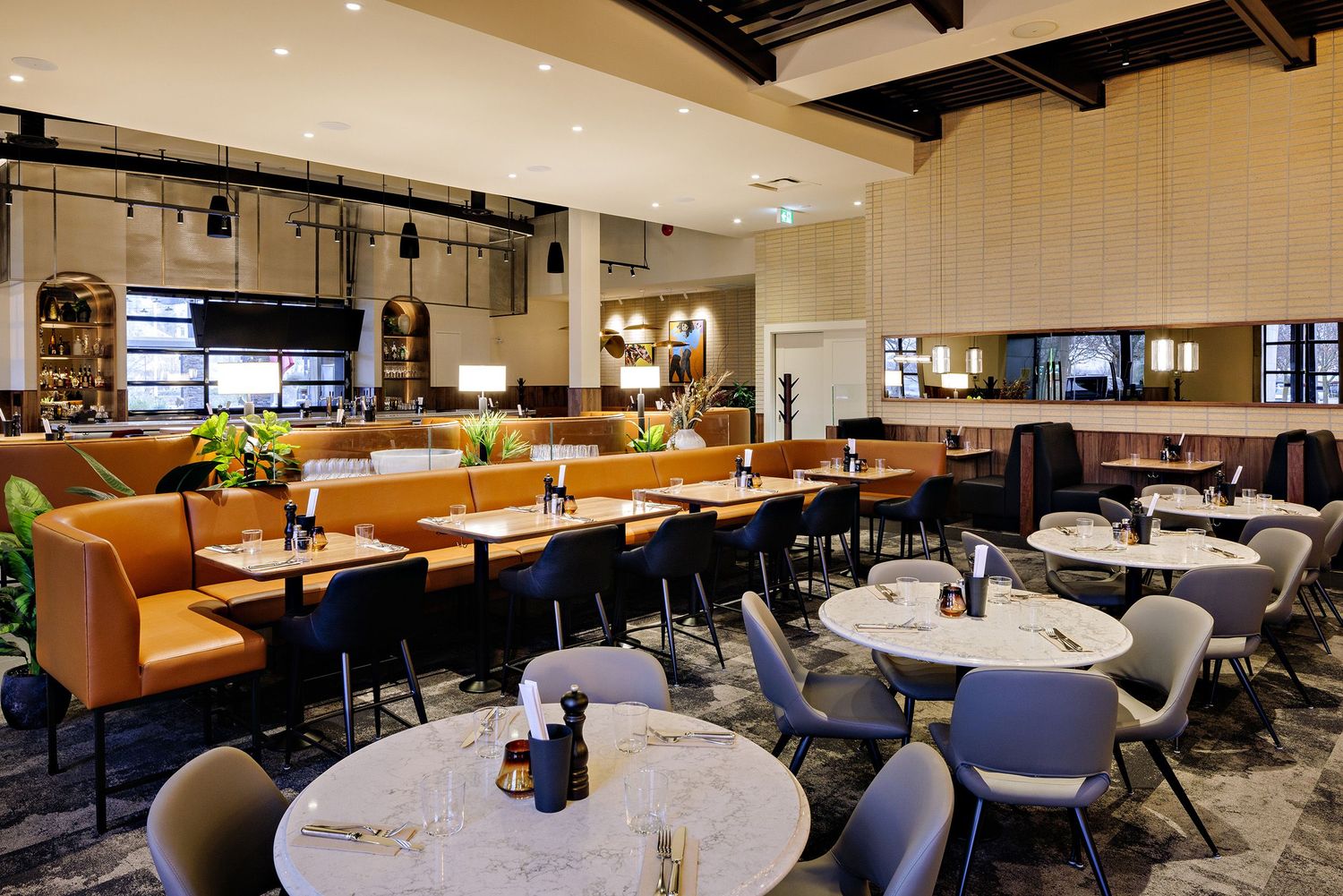 Modern restaurant interior with orange leather booths, white marble tables, and contemporary gray chairs in an upscale setting.