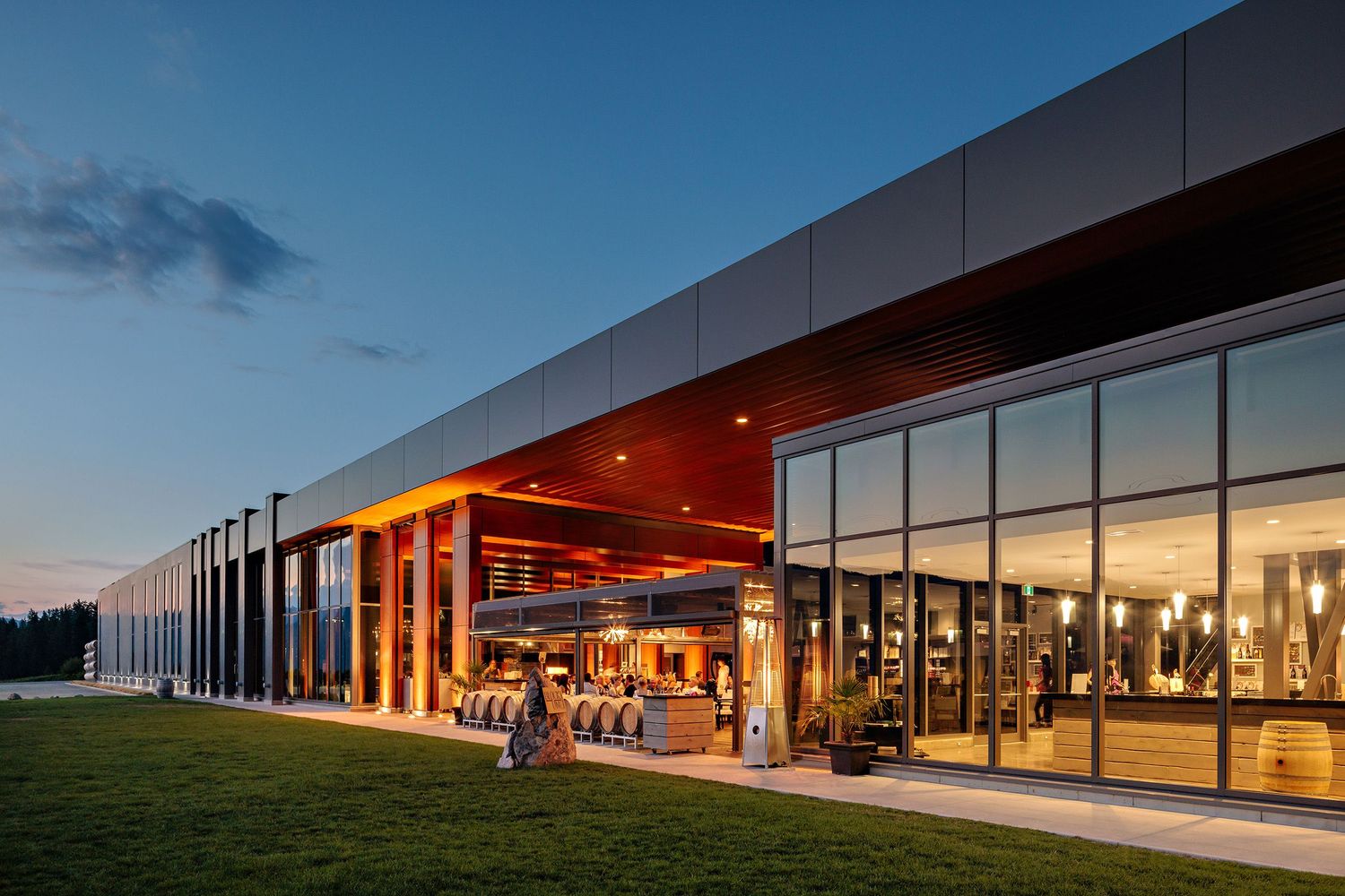 Modern commercial building exterior with glass windows and red illuminated overhang at dusk displays warm interior lighting.