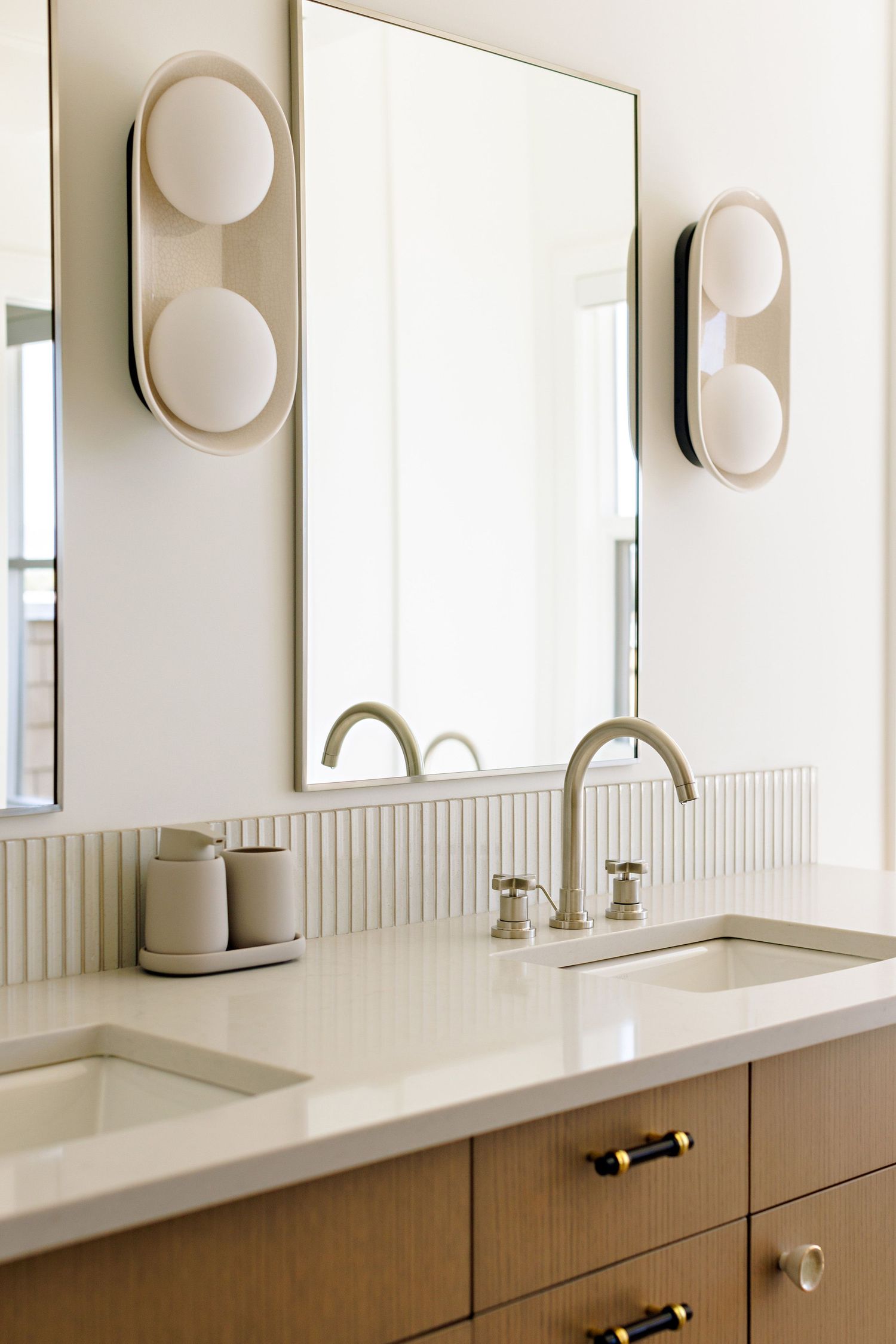 Modern bathroom vanity with double sinks, wooden cabinets, and circular wall sconces.