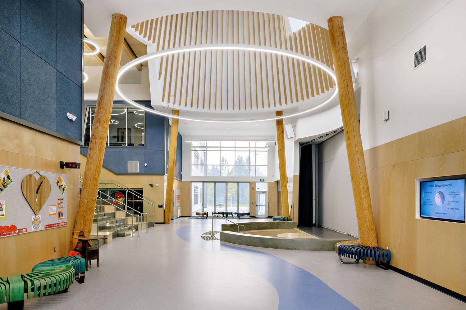 Modern school lobby interior with circular lighting fixture, wooden columns, and blue accent wall features clean minimalist design.