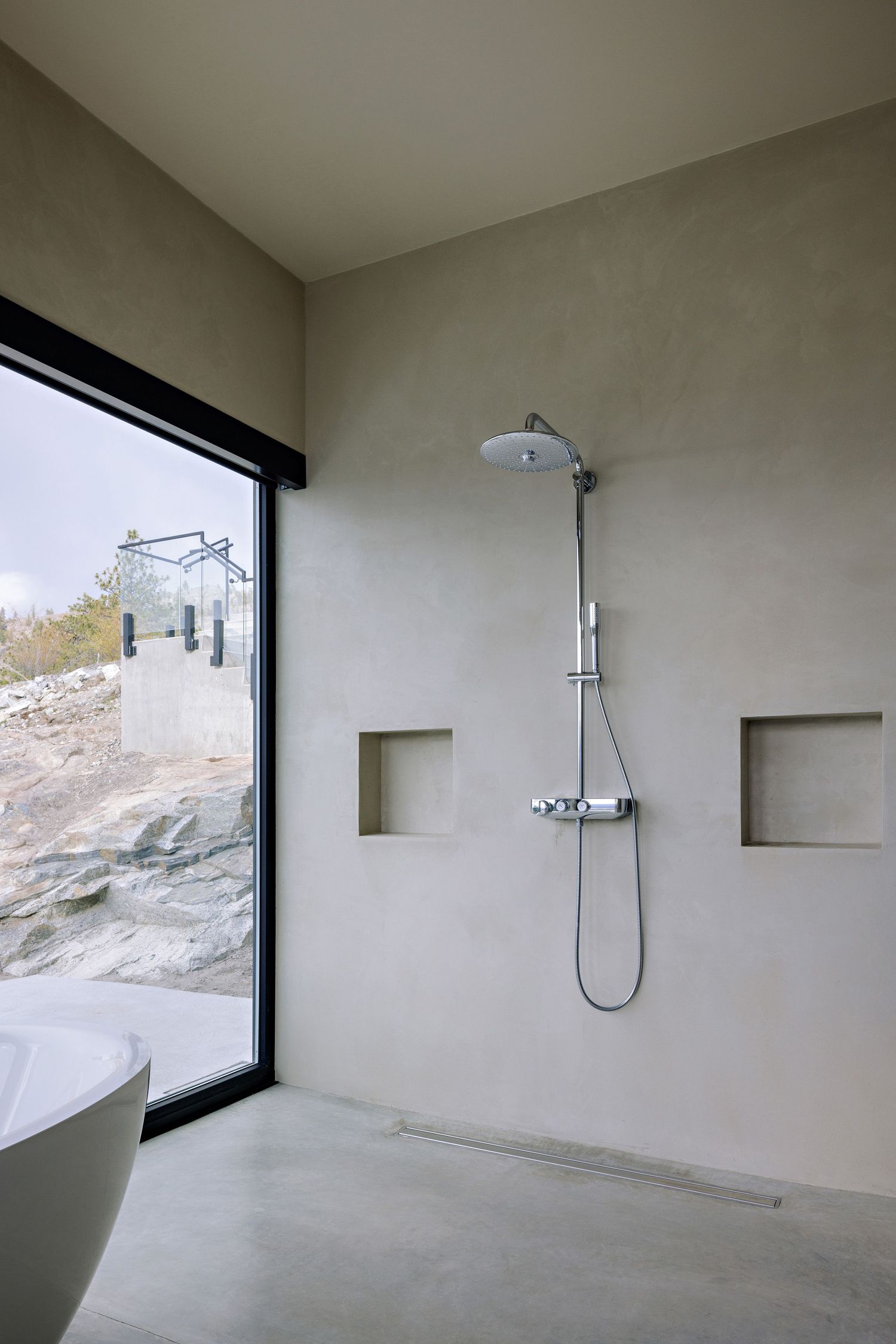 Modern minimalist bathroom with a glass window shower featuring built-in wall niches and a view of rocky terrain outside.